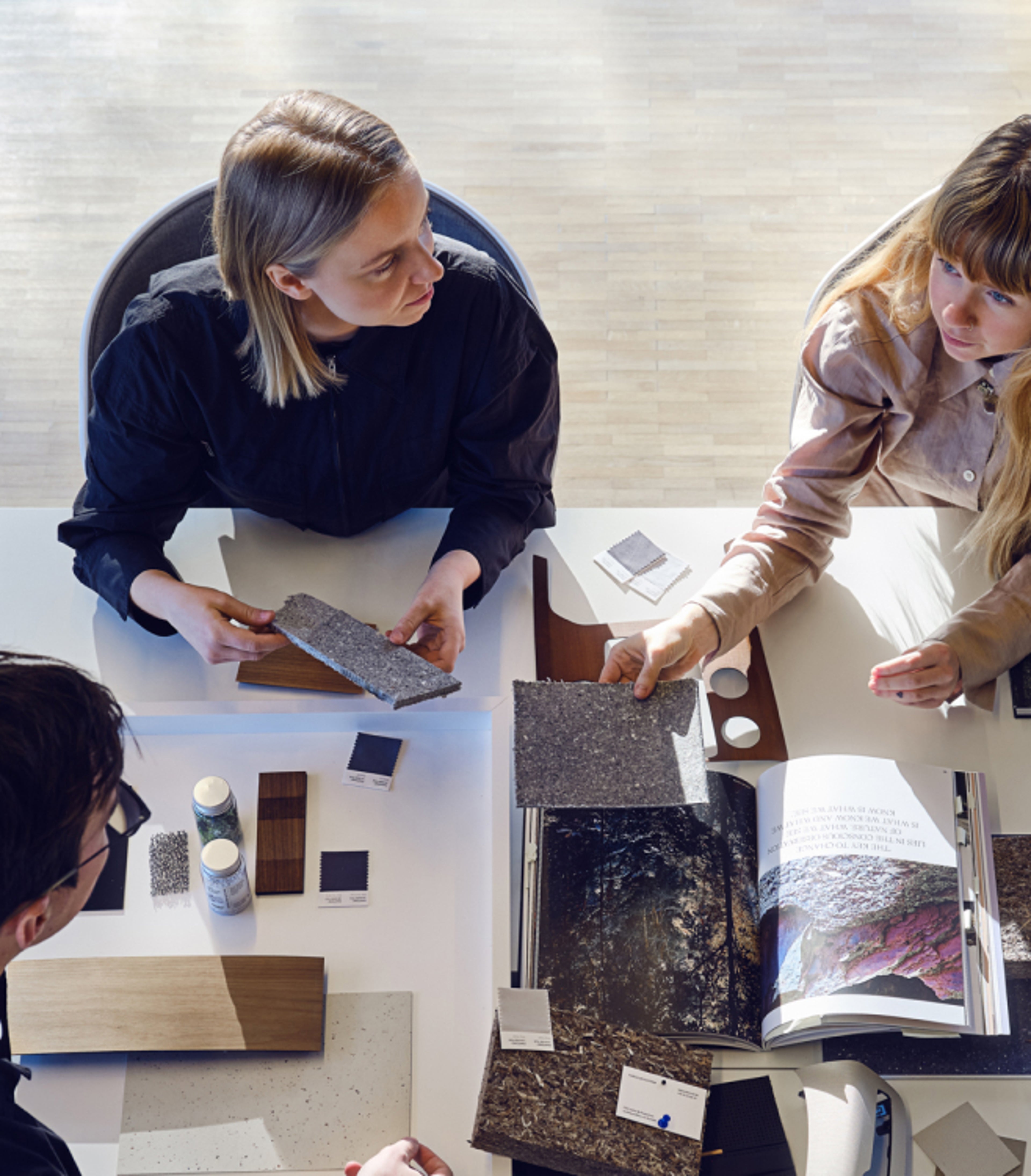 Deux femmes et un homme assis autour d'une table discutant des matériaux sur la table.