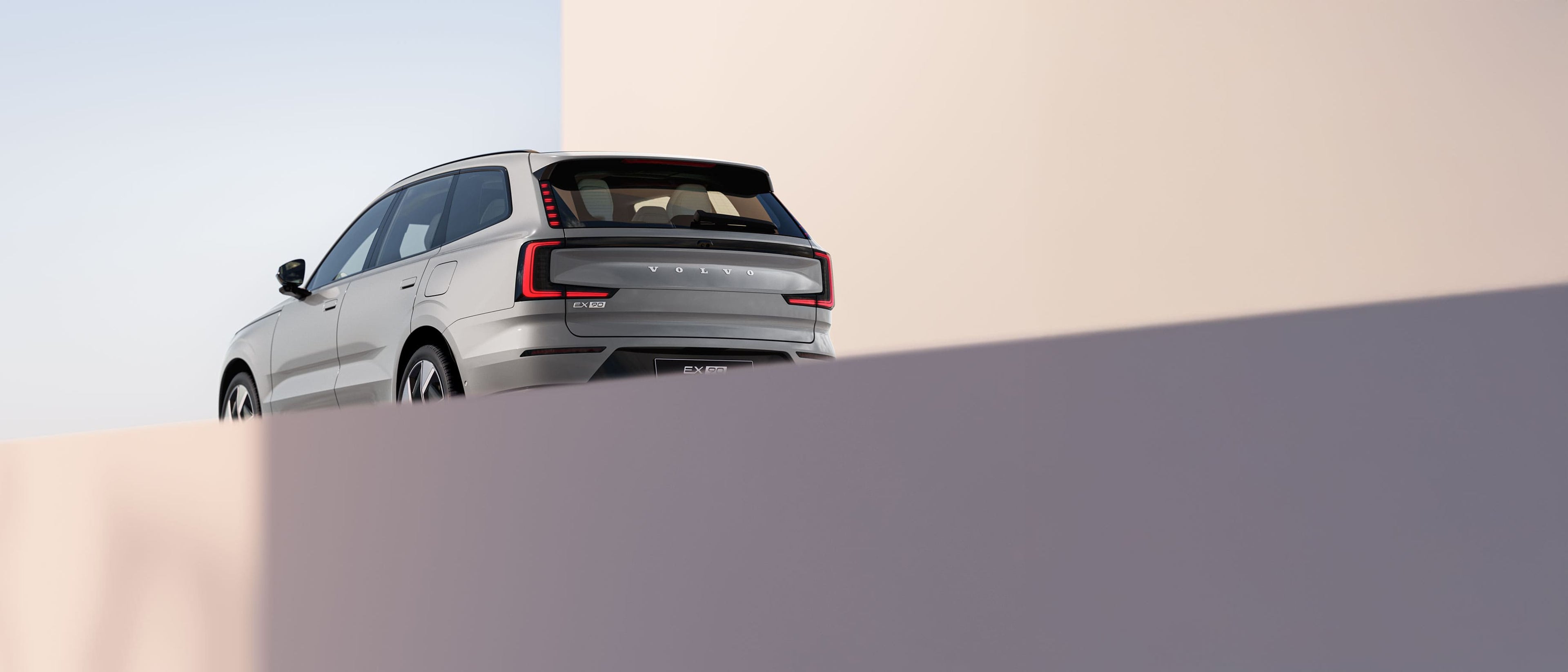 מבט מאחור על רכב SUV כסוף מדגם וולוו EX90 חונה בסביבת מבנה מינימליסטי.