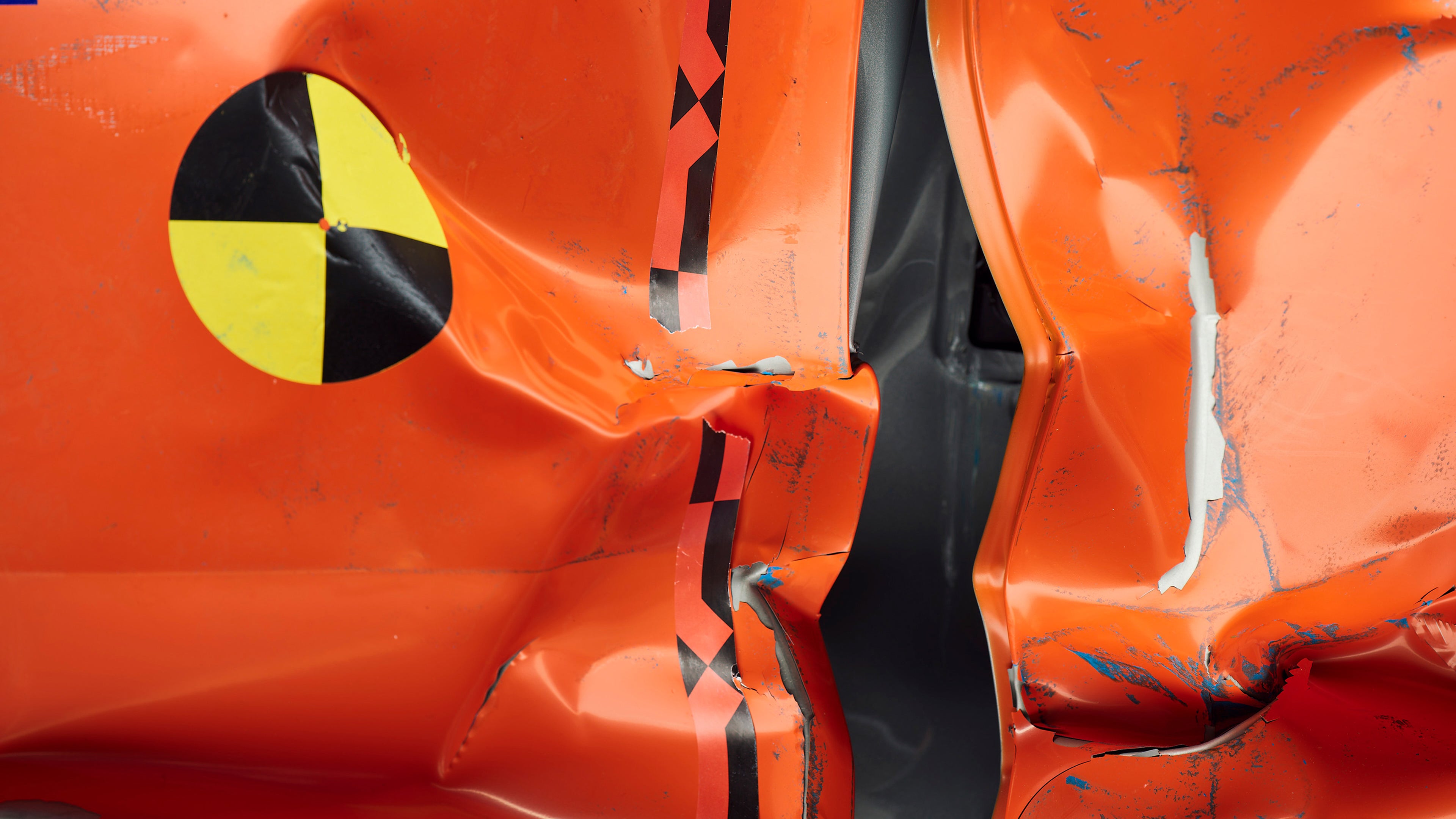 Primo piano di pannelli metallici arancio frantumati con segni di vernice blu lasciati da un impatto.