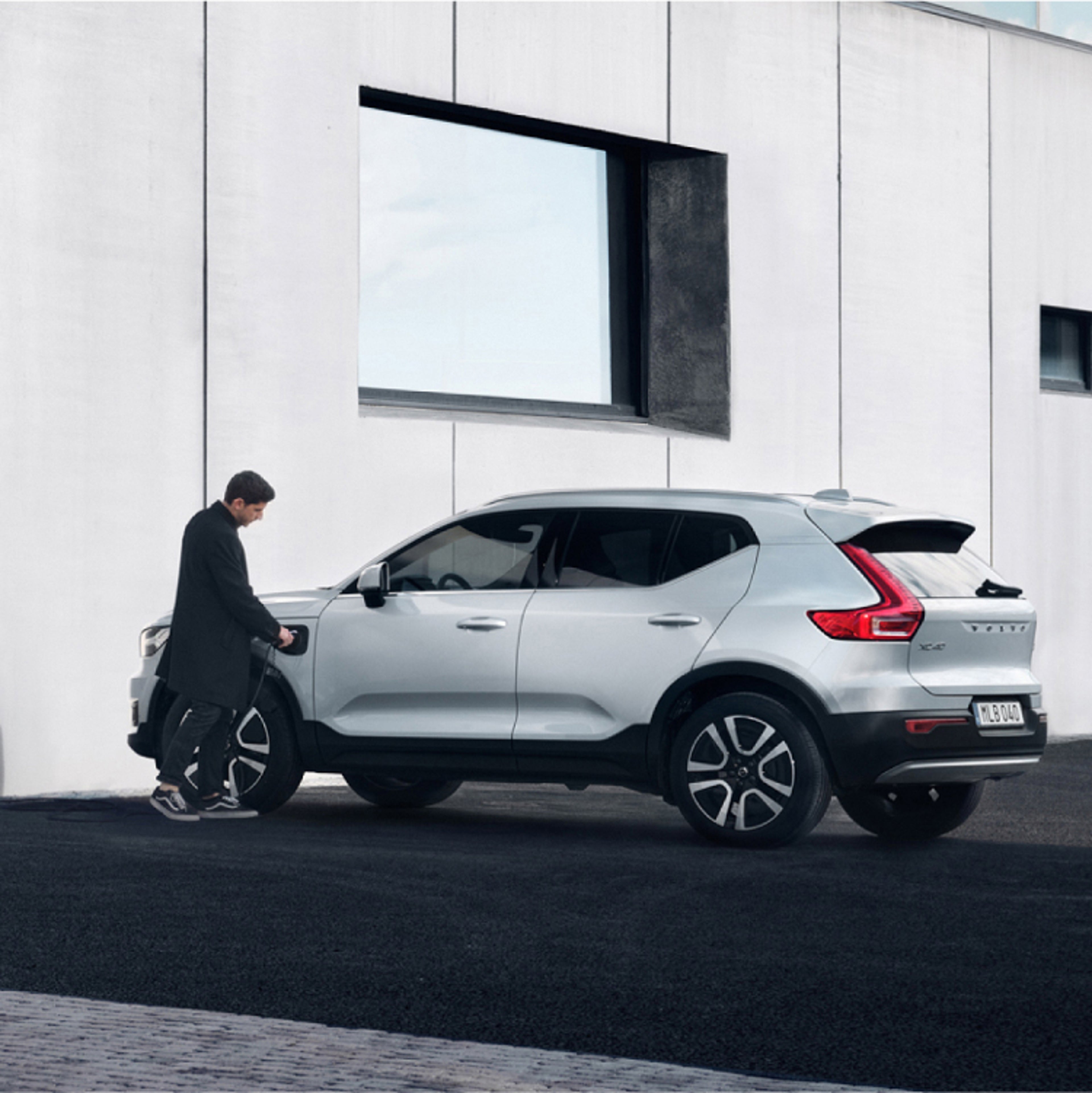 A man plugging a wall charger into a grey Volvo XC40 that’s parked by a charging station