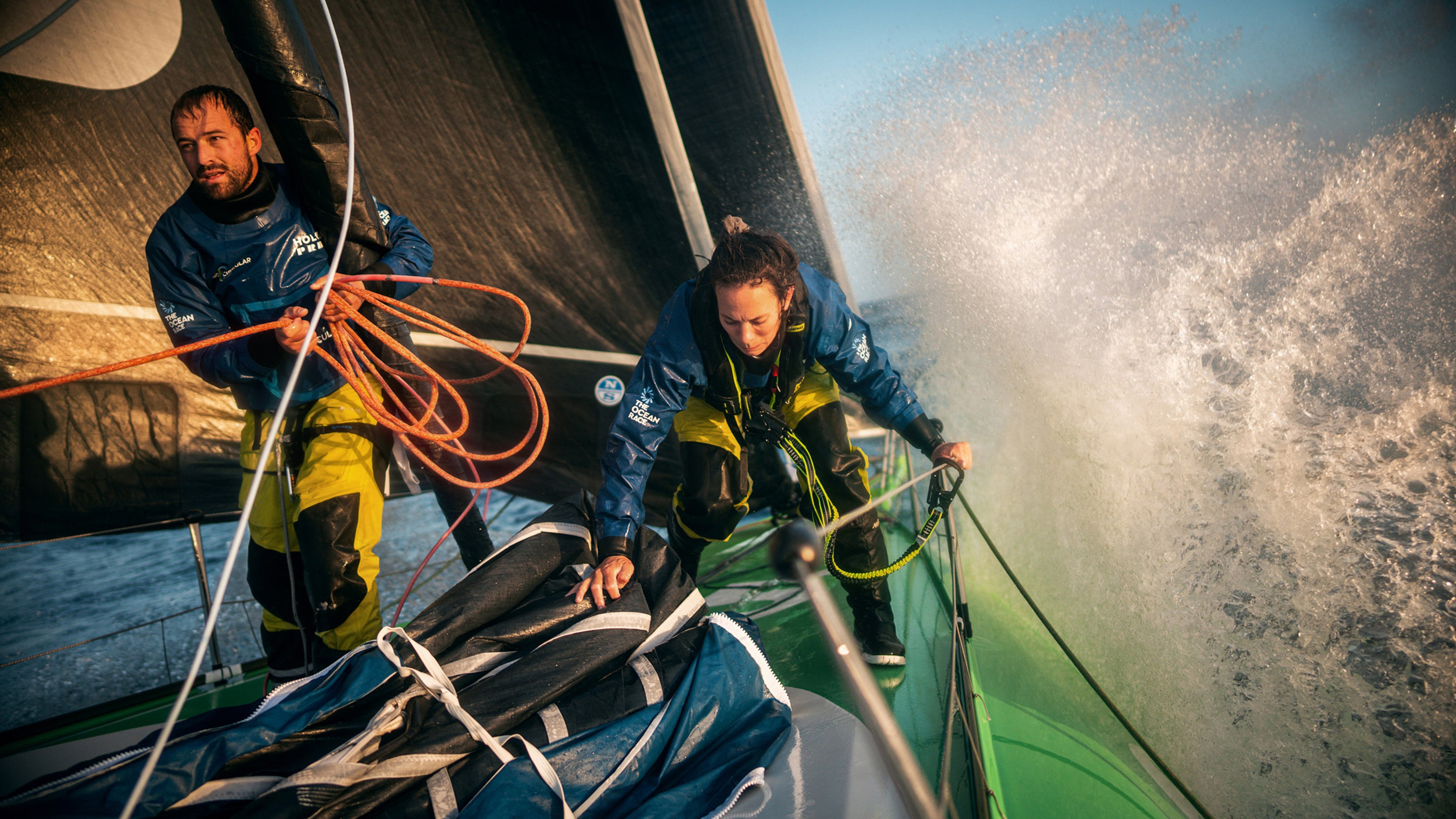 Dva mornara u vodootpornoj opremi upravljaju regatnom jahtom kroz nemirno more tokom takmičenja The Ocean Race.