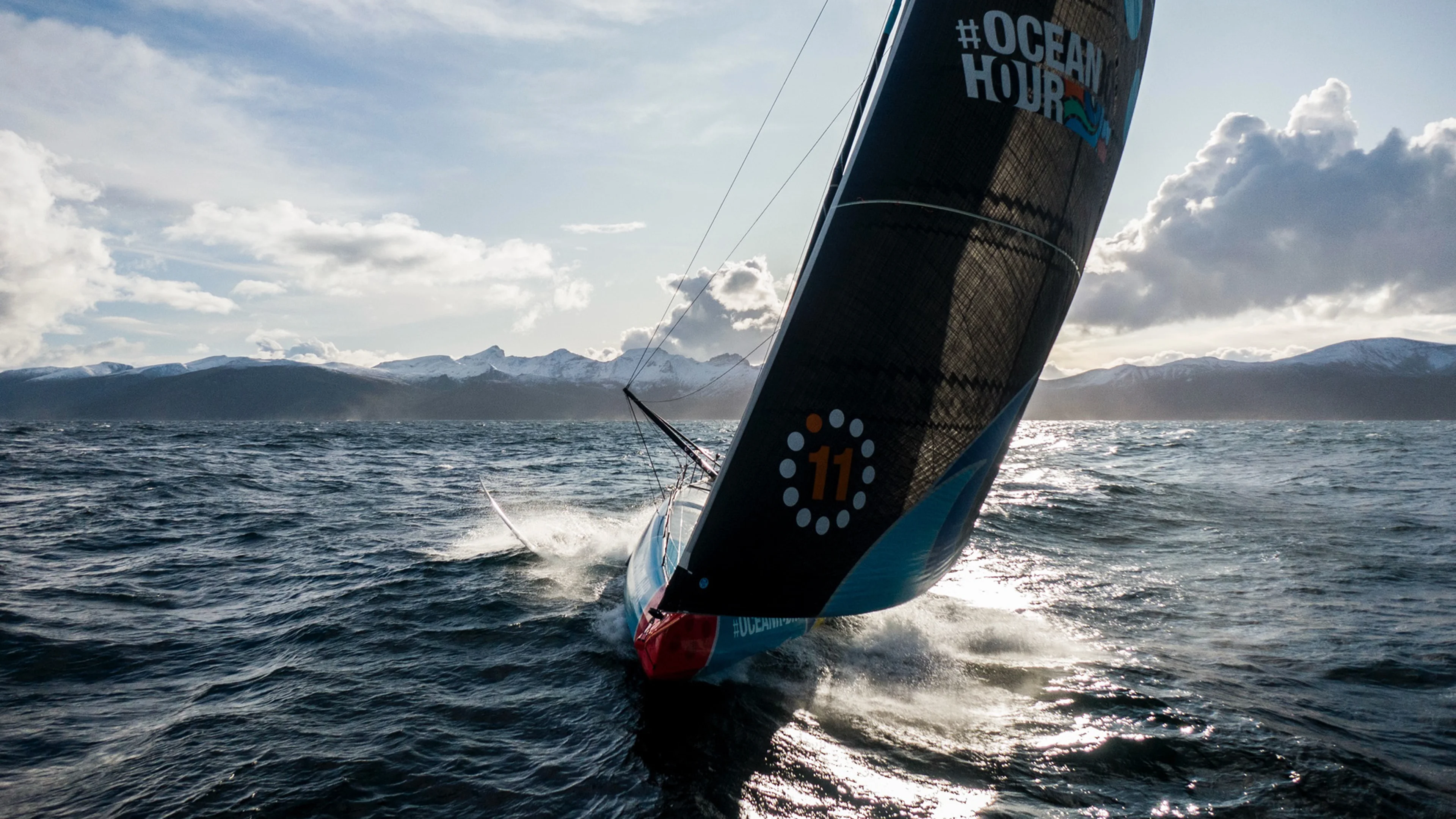 A high performance sailboat racing through open ocean waters under dramatic skies, featuring The Ocean Race branding.