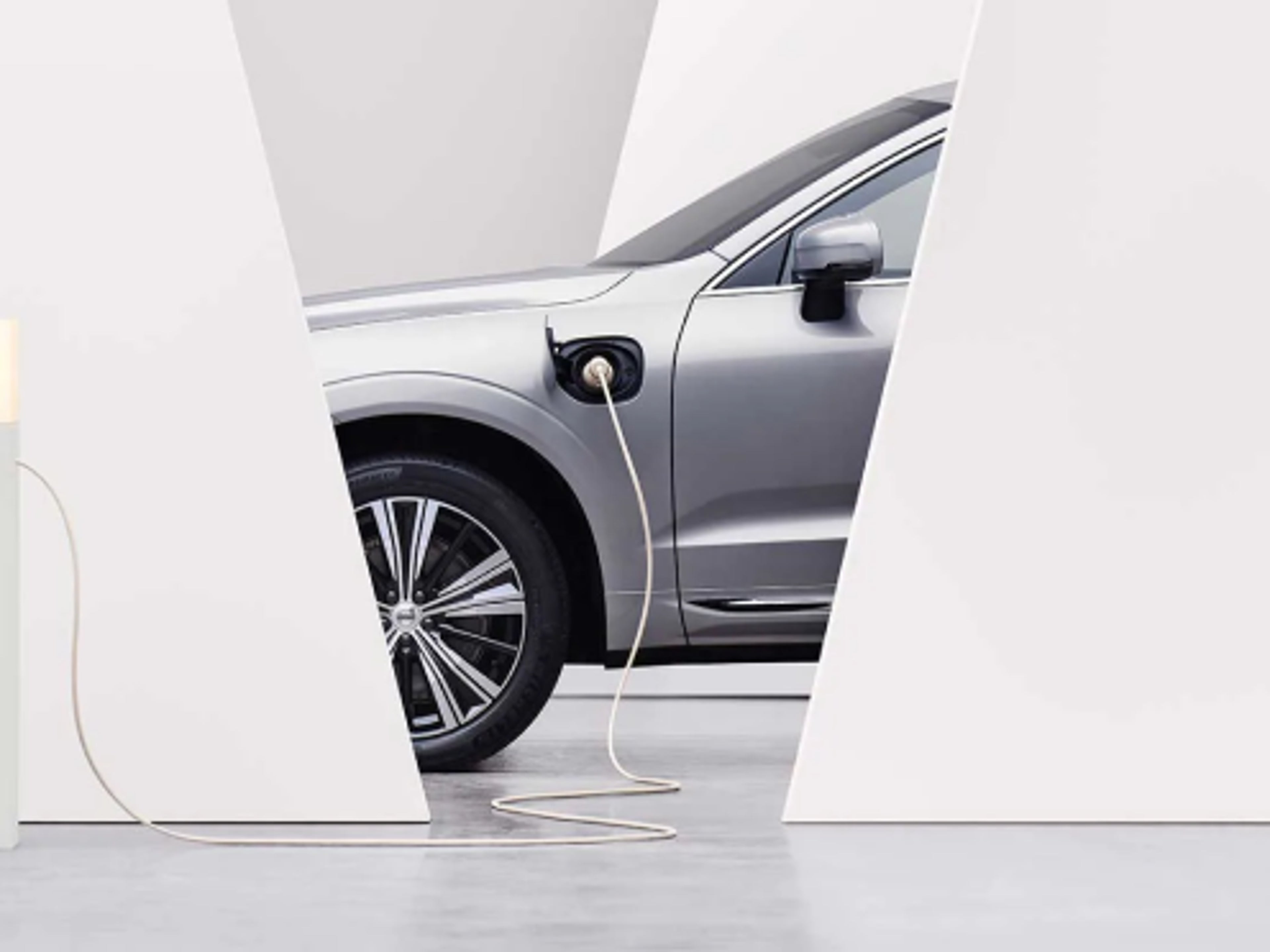A partial side-view of a Volvo car with a plugged-in charger.