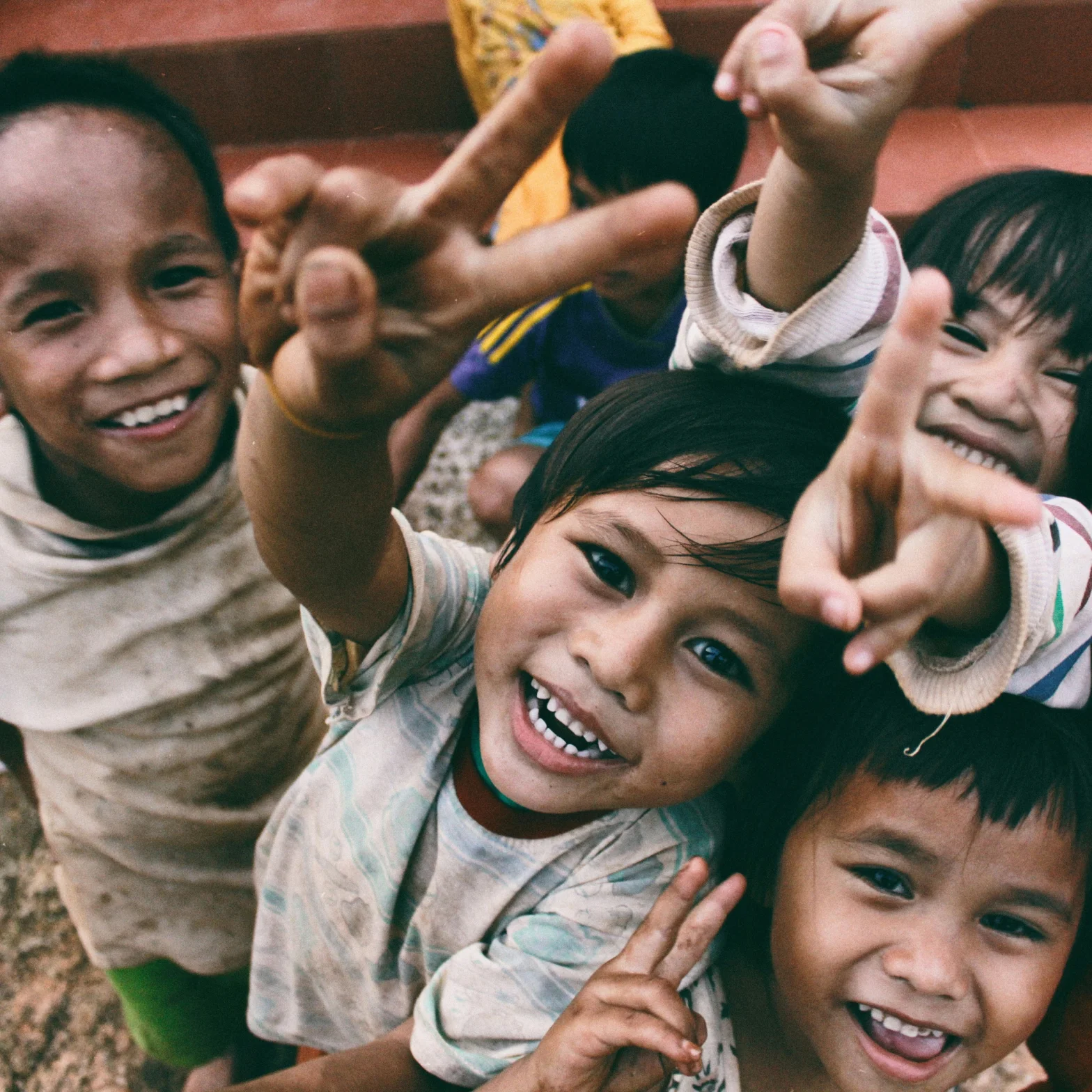 Group of joyful children smiling and making peace signs with their fingers.