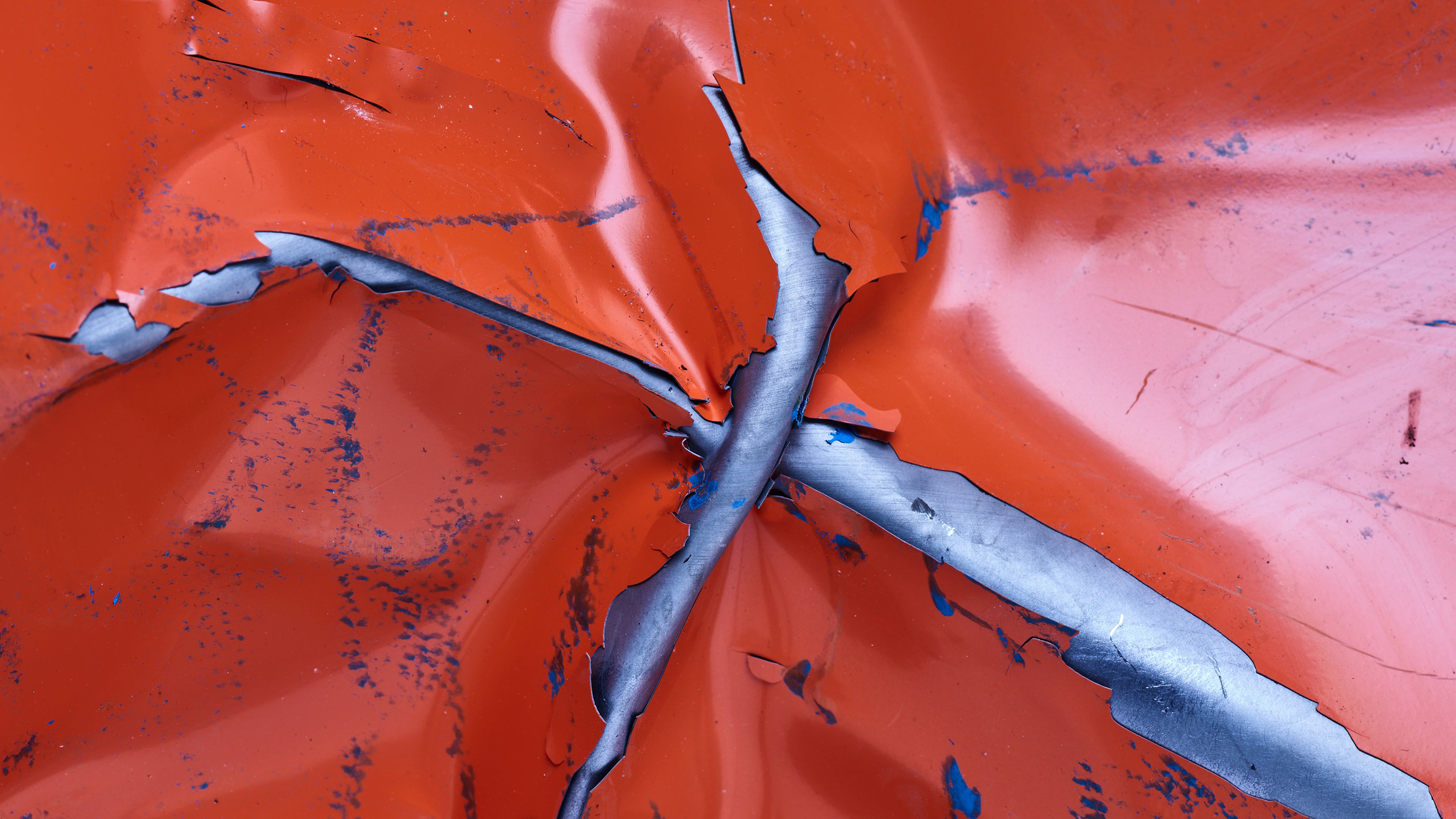 Primo piano di metallo arancio reciso e contorto con acciaio vivo esposto e segni di vernice blu.