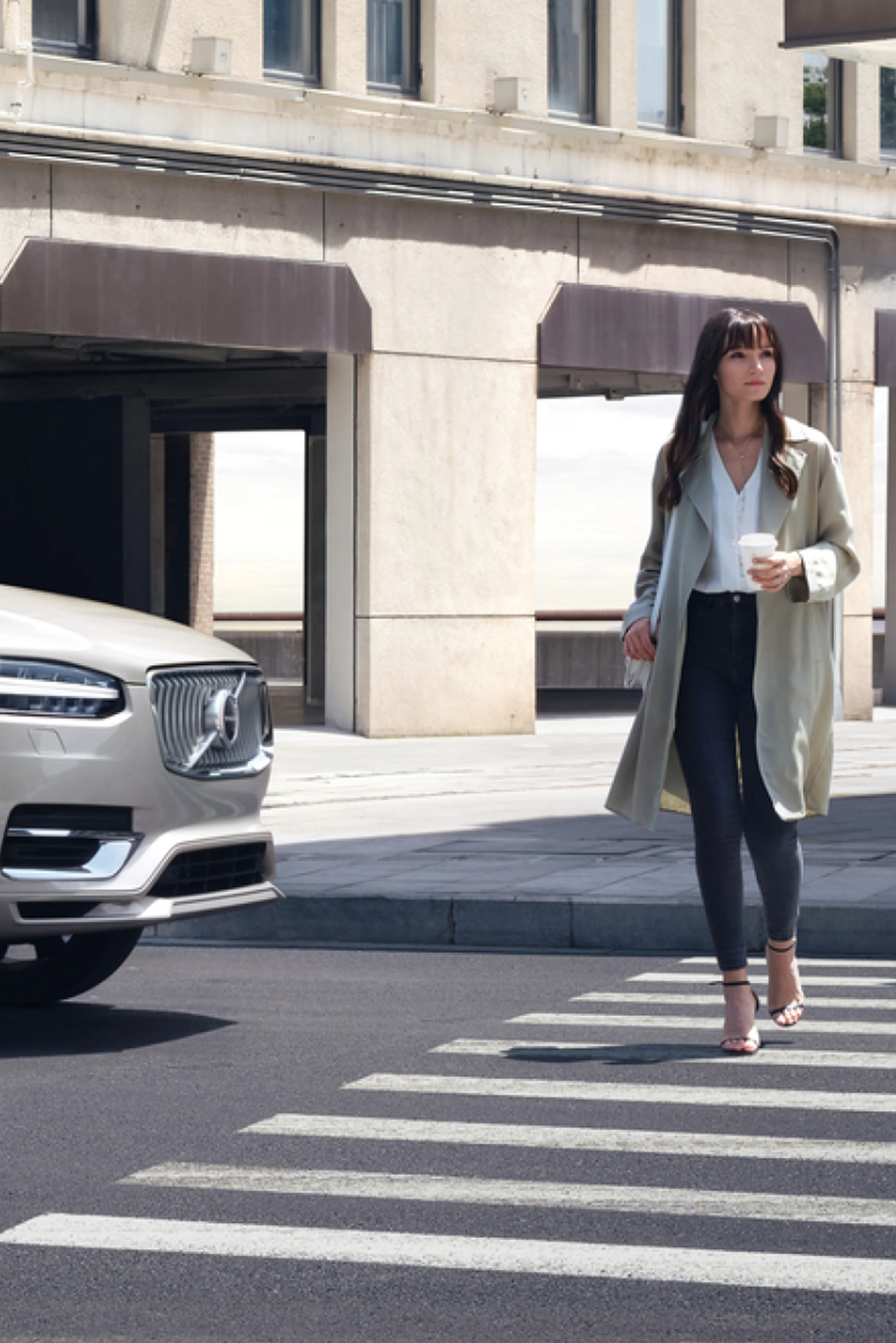 Volvo XC90 stoppar við gangbraut á meðan kona með kaffibolla í hönd gengur yfir.