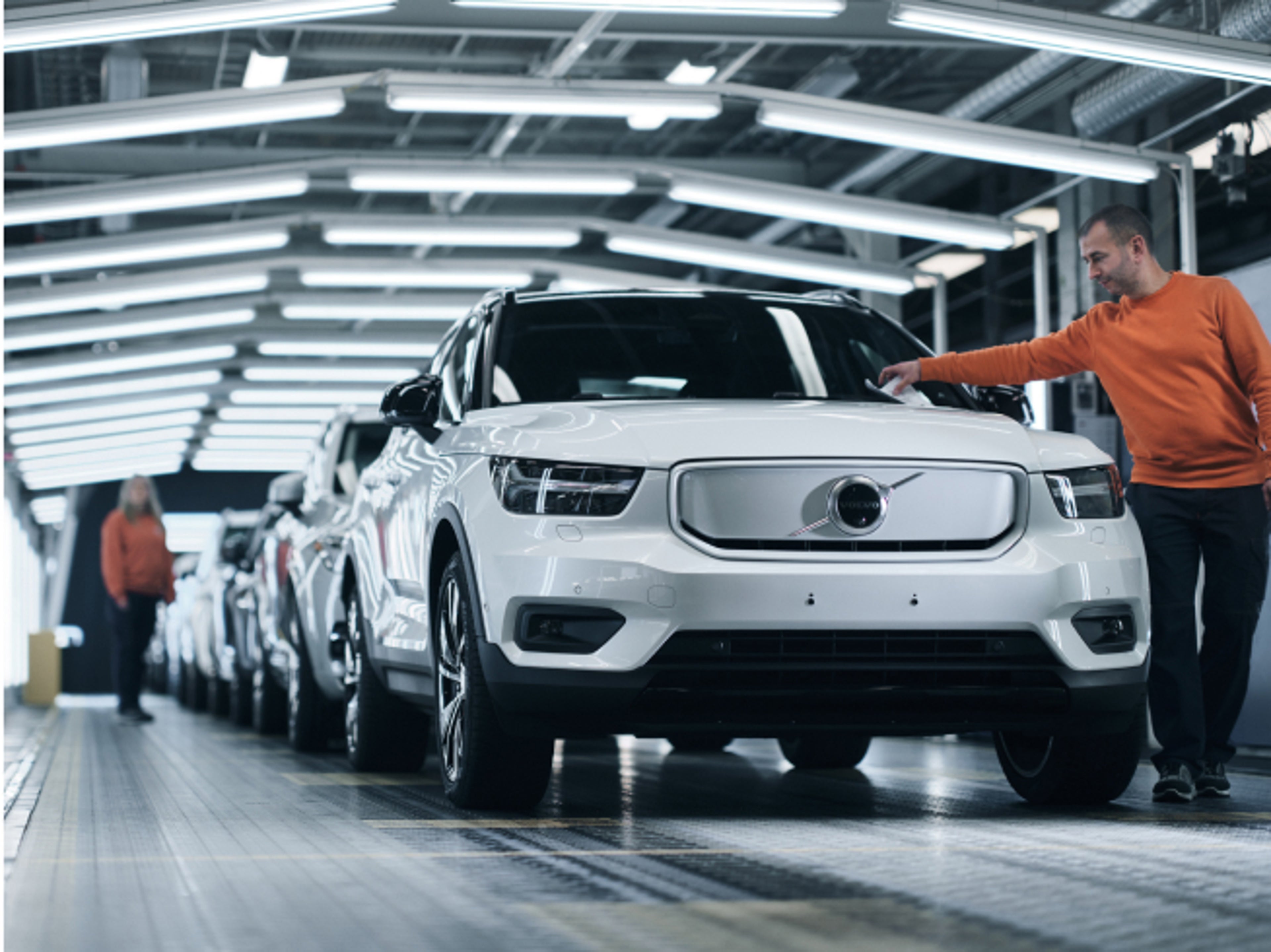 A man checking new Volvo XC40 cars on a conveyor belt inside a manufacturing plant.