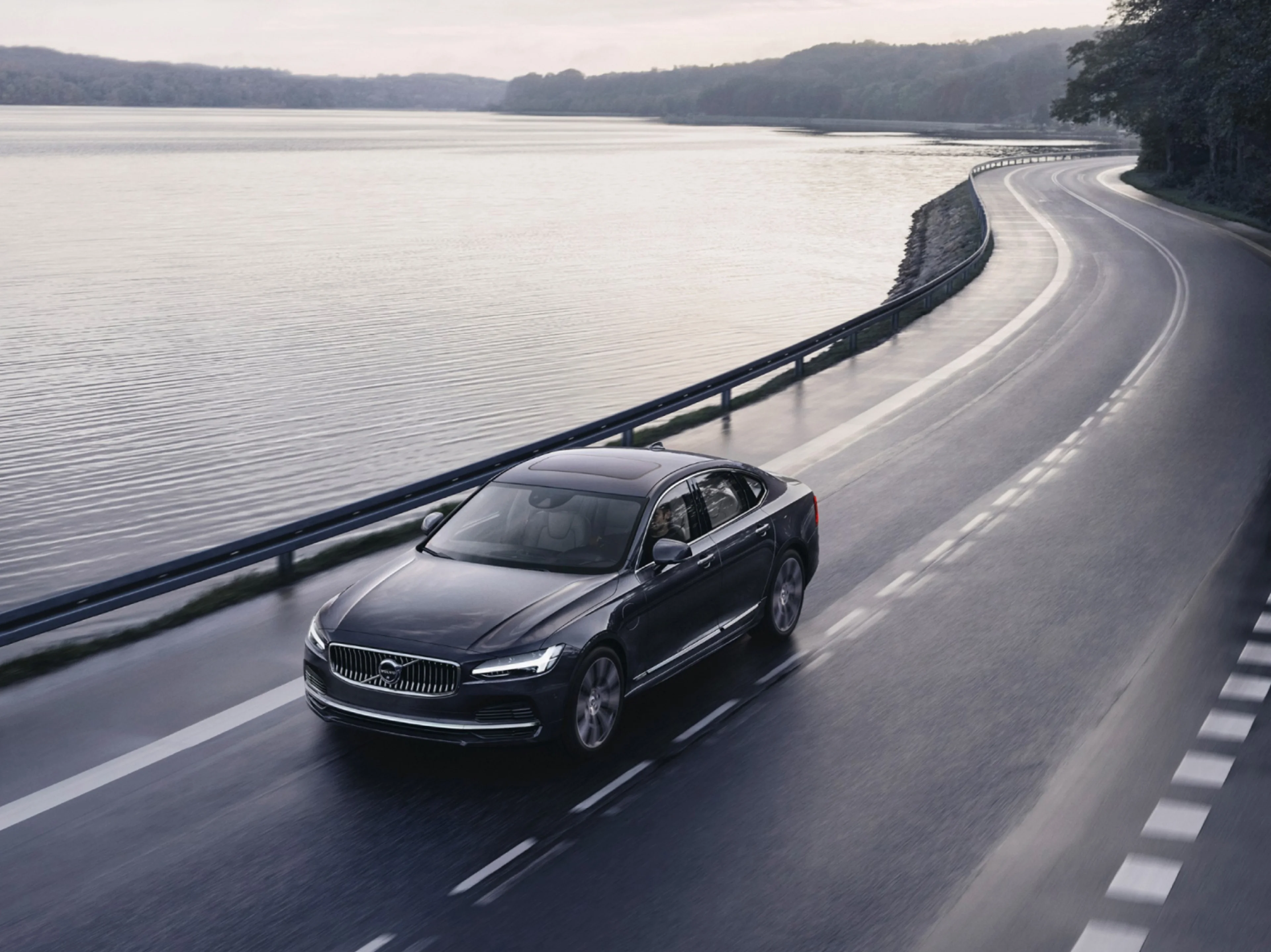 A Volvo car driving on a road that borders a lake.