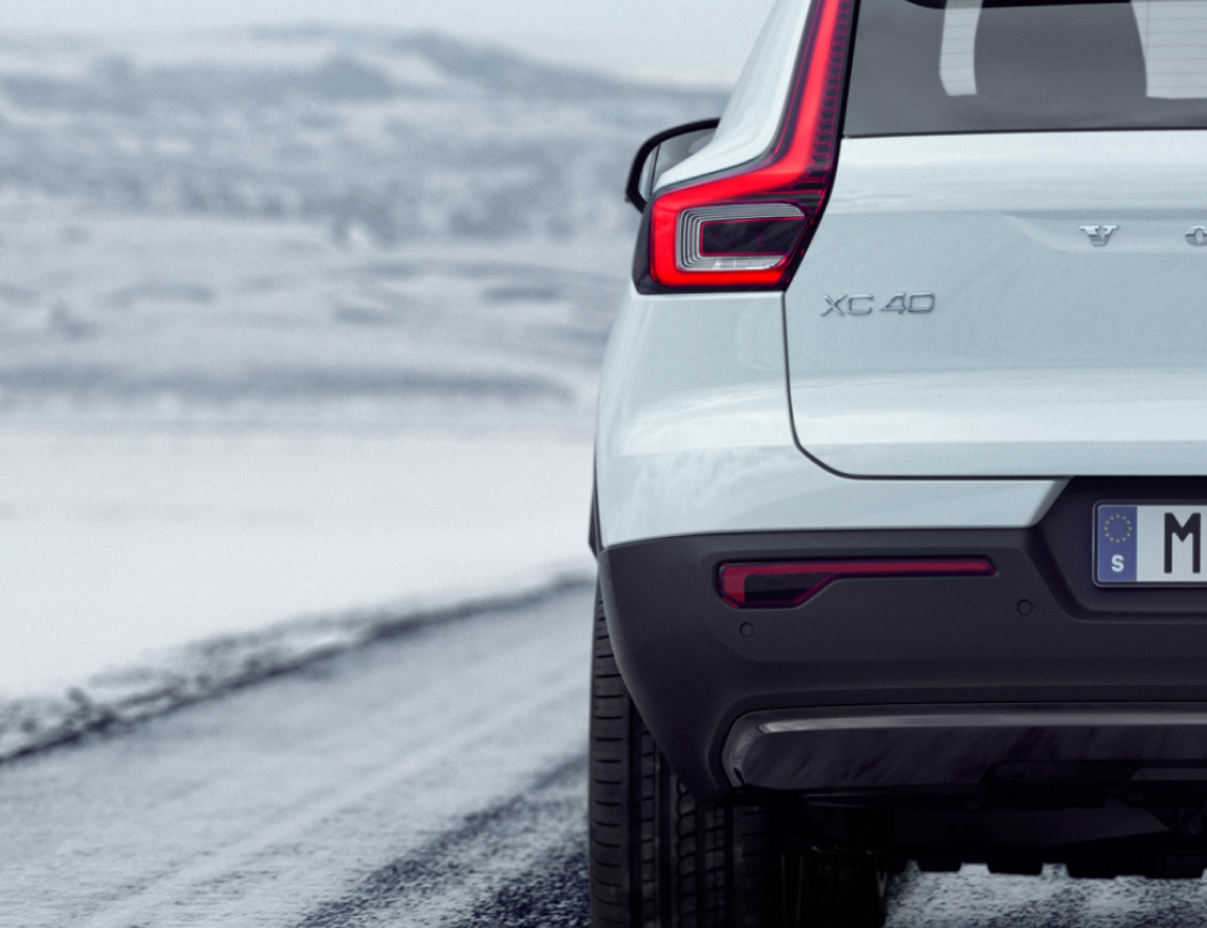 Valkoinen Volvo XC40 ajaa jäisellä tiellä osittain takaa kuvattuna.