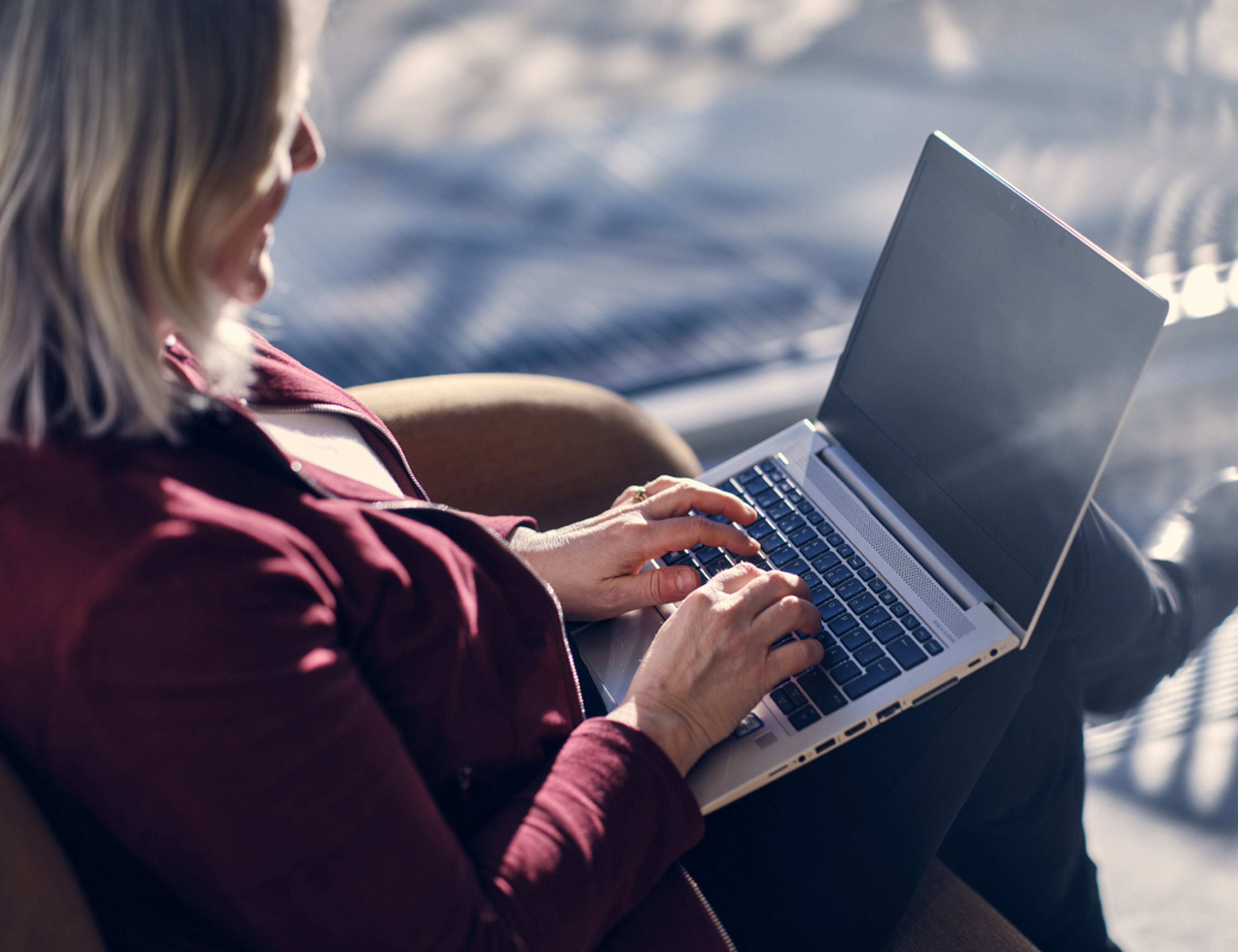 Kuva ylhäältä päin naisesta, joka istuu sohvalla ja tekee töitä kannettavalla tietokoneella.