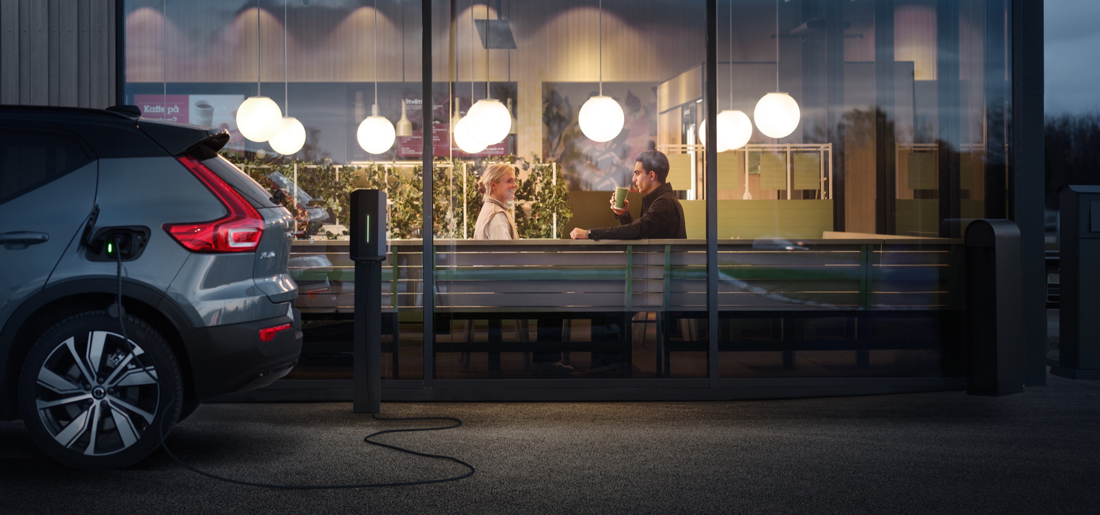 Egy XC40 hátsó részének részleges nézete töltés közben, amint egy kávézó előtt parkol, ahol két ember ül egymással szemben.