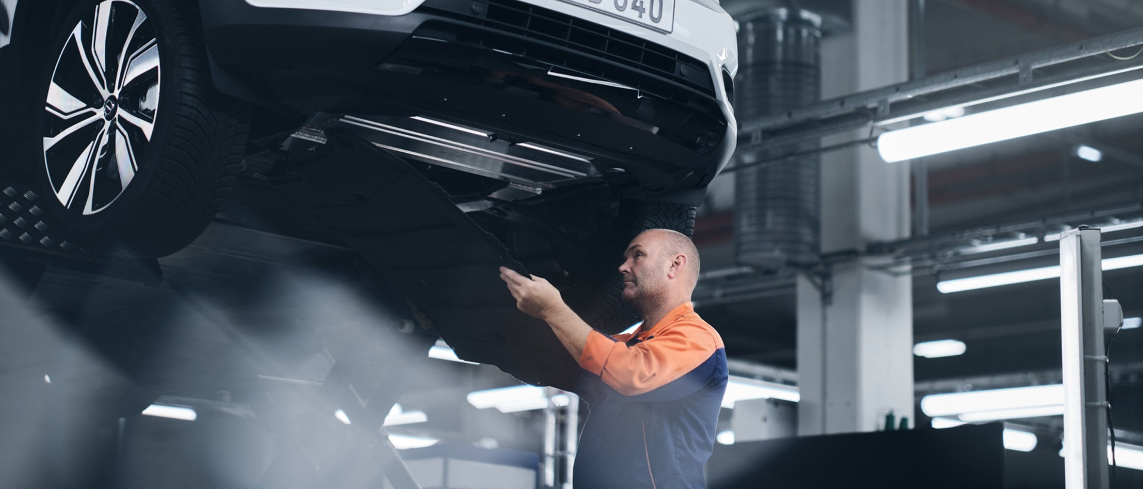 Homme travaillant sous une voiture surélevée.