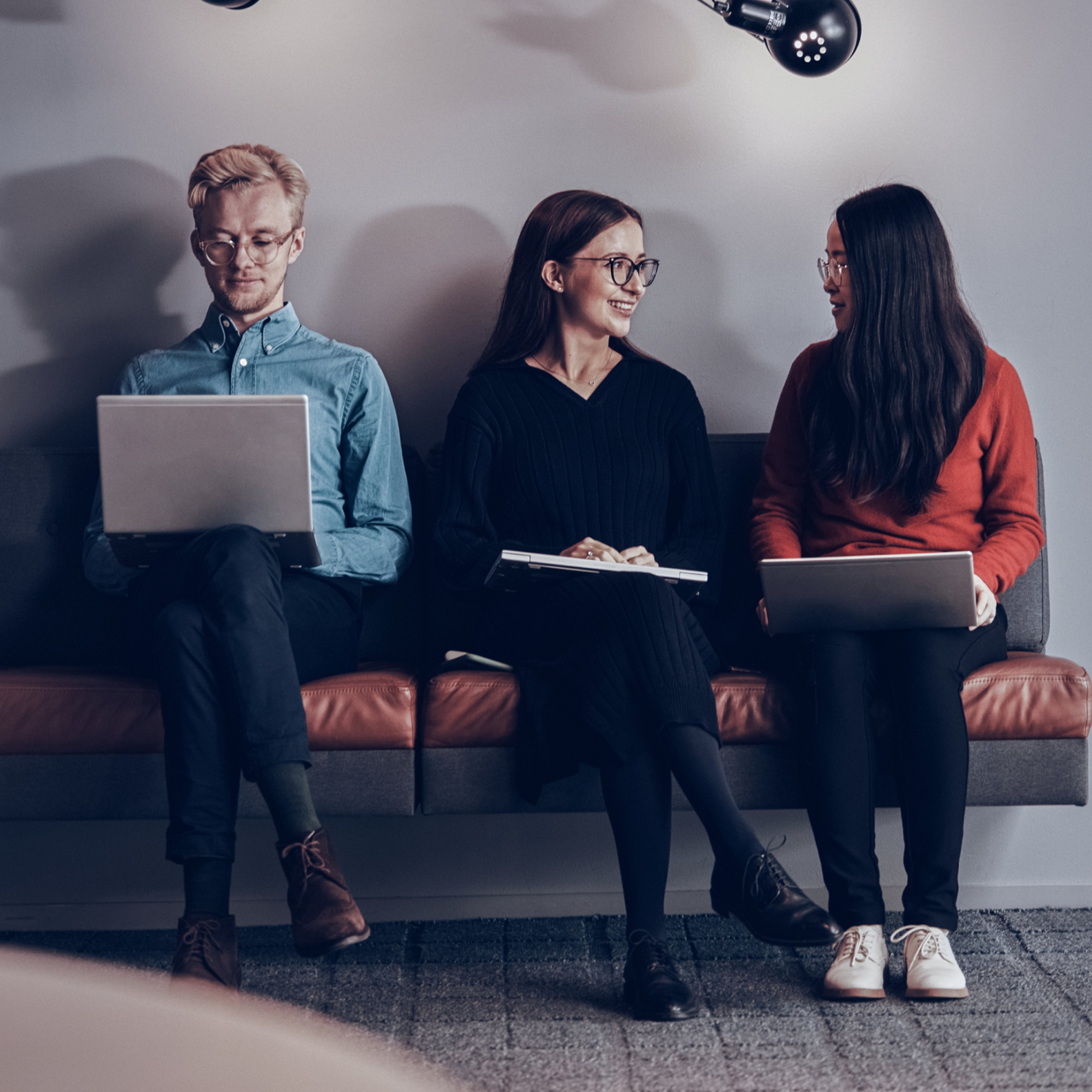 Two females and one male sat on a sofa holding their laptops.