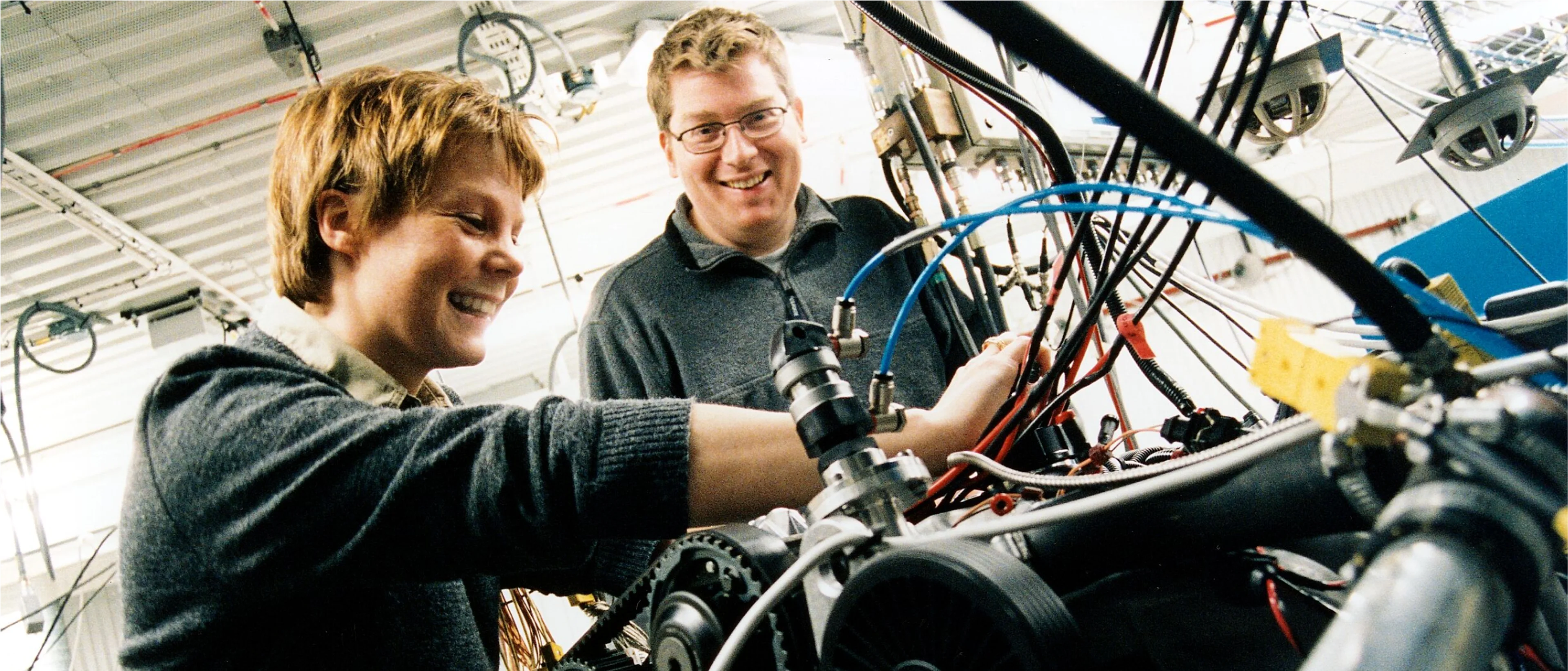 A man and a woman smiling while they work on a motor in a Volvo Car manufacturing plant.