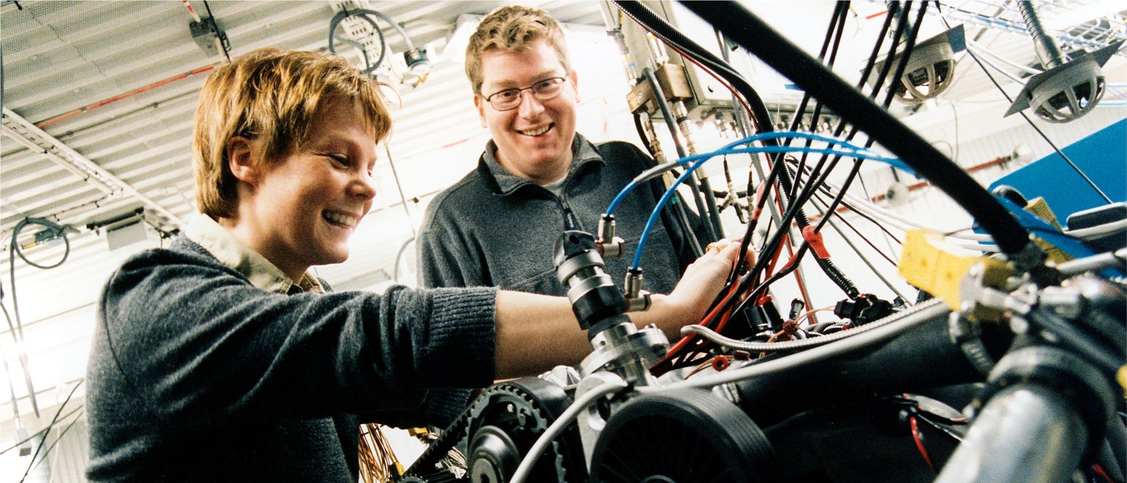 A man and a woman smiling while they work on a motor in a Volvo Car manufacturing plant.