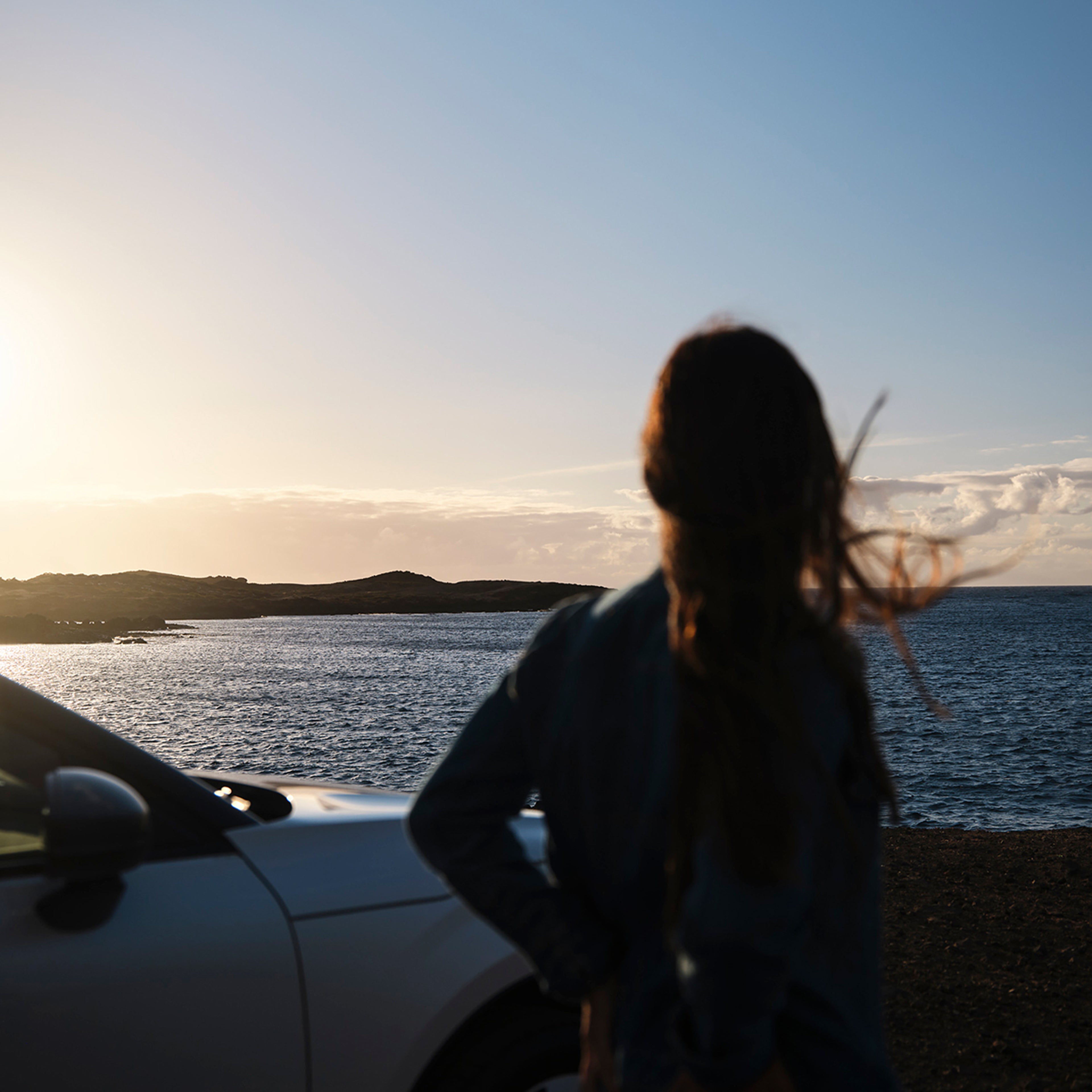 Žena stoji pored Volvo automobila i gleda u horizont okeana tokom zalaska sunca. Simbolizuje posvećenost kompanije Volvo zdravlju okeana i partnerstvu sa The Ocean Race.