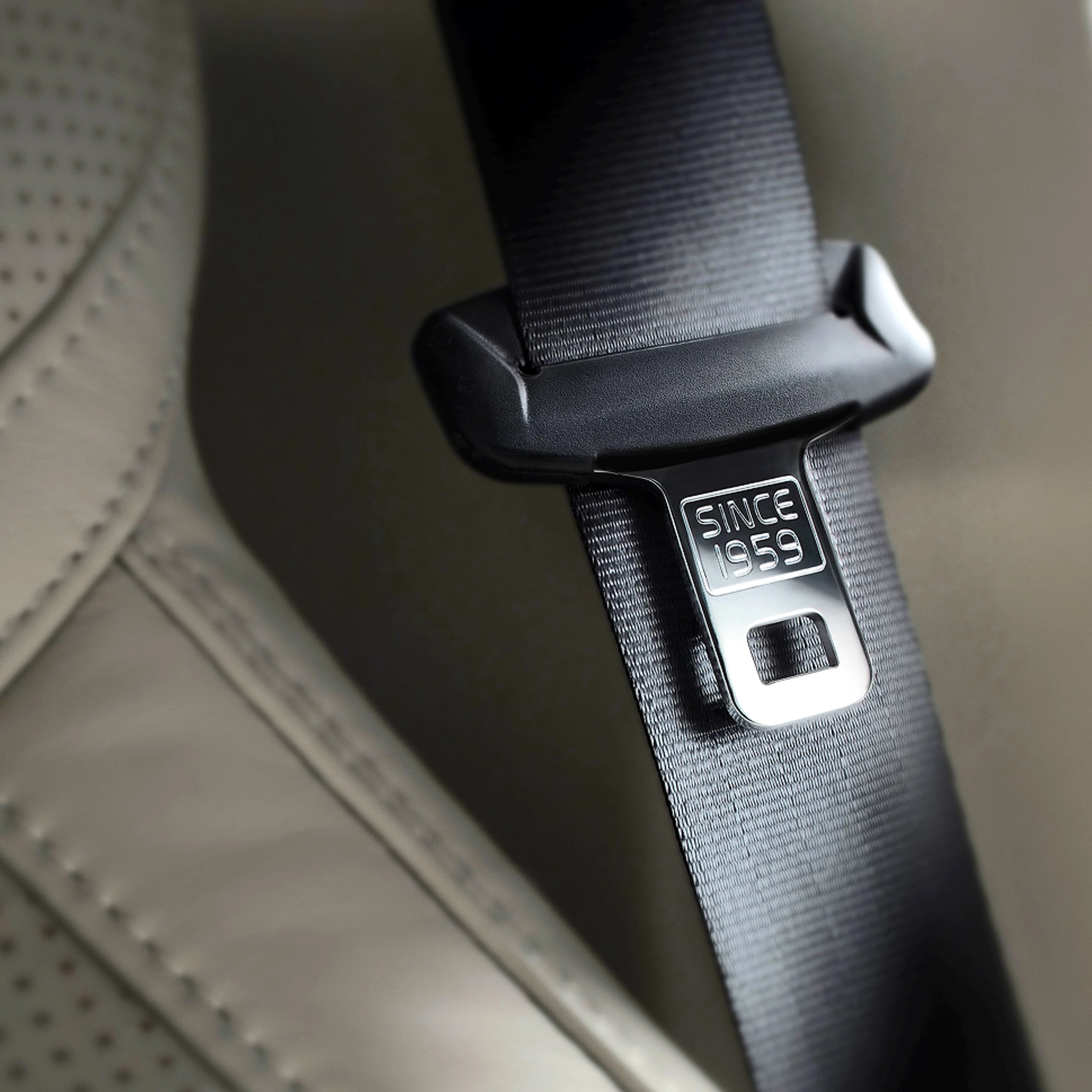 Zbliżenie na klamrę trzypunktowego pasa bezpieczeństwa z wygrawerowanym napisem "SINCE 1959" na skórzanym wnętrzu samochodu.