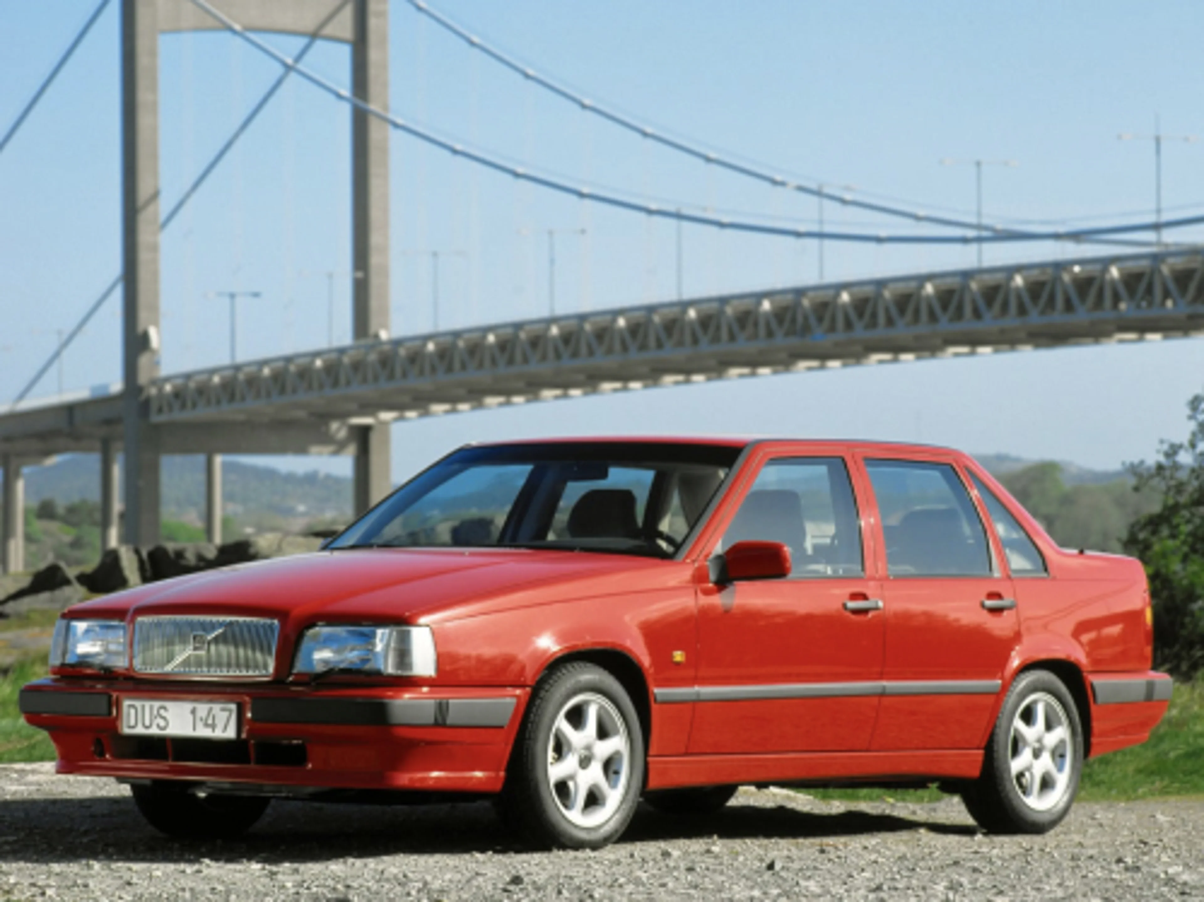 Un Volvo 850 rojo aparcado frente a un puente.