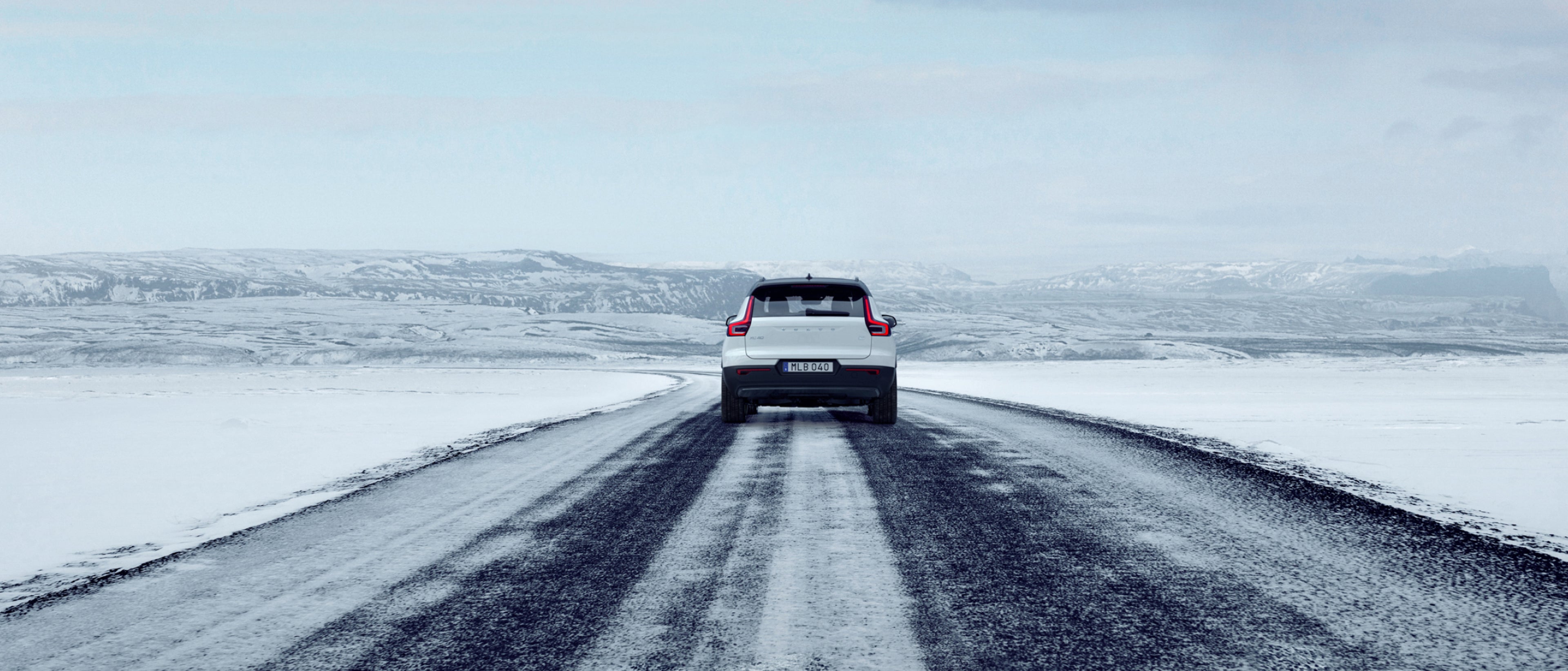 Valkoinen Volvo XC40 ajaa jäisellä tiellä takaa kuvattuna.