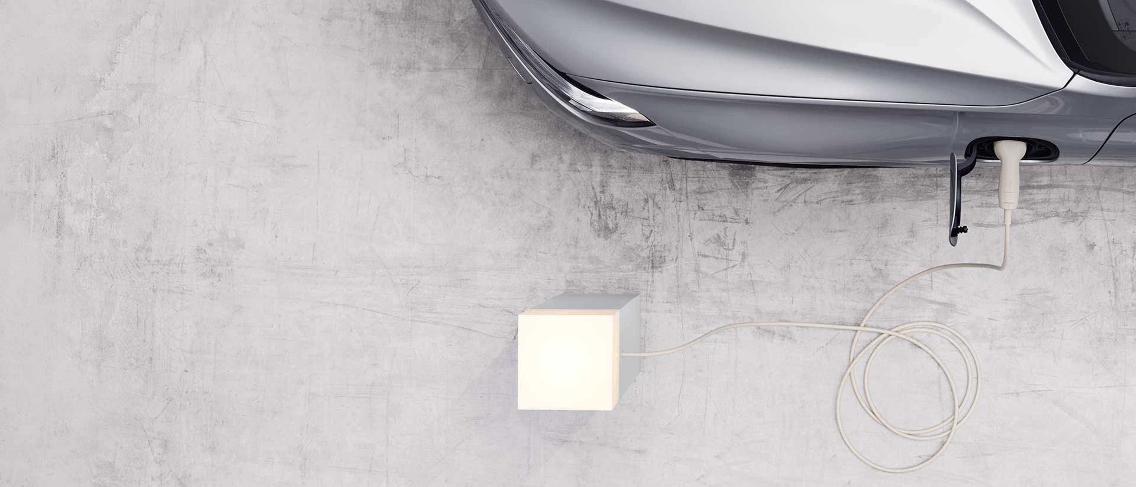 Top-down partial view of a Volvo charging from an outlet that’s lit up.