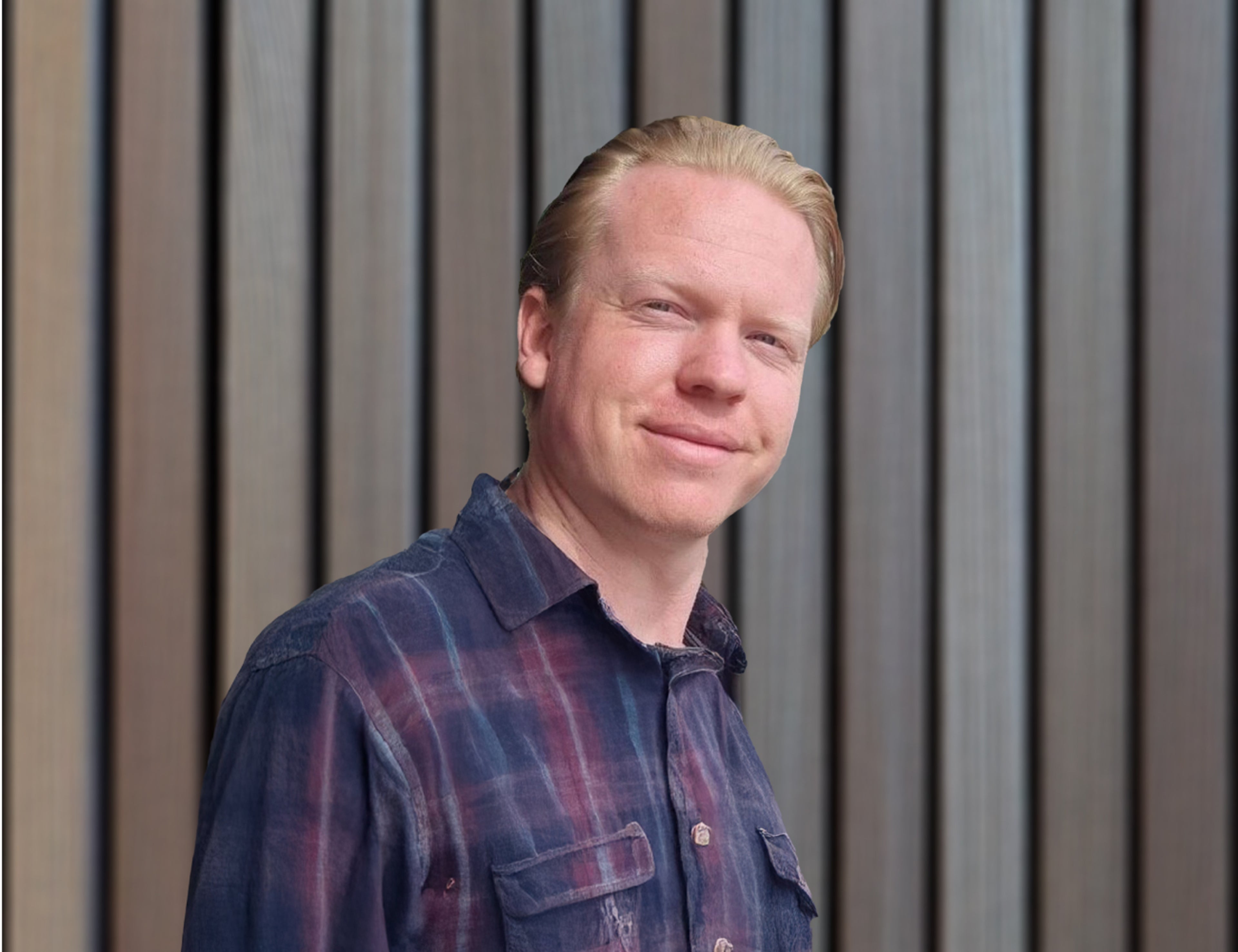 En person som bär en blå och röd rutig skjorta står framför en modern vertikal lamellvägg i trä, vilket skapar en modern och avslappnad atmosfär.