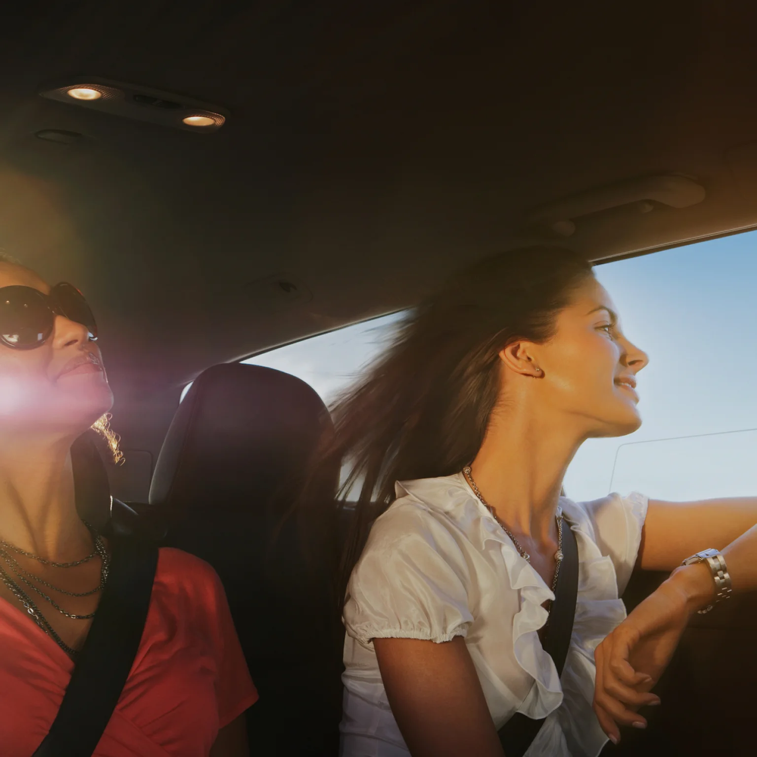 Femme regardant par la fenêtre d’une voiture depuis un siège passager, le vent soufflant dans ses cheveux.