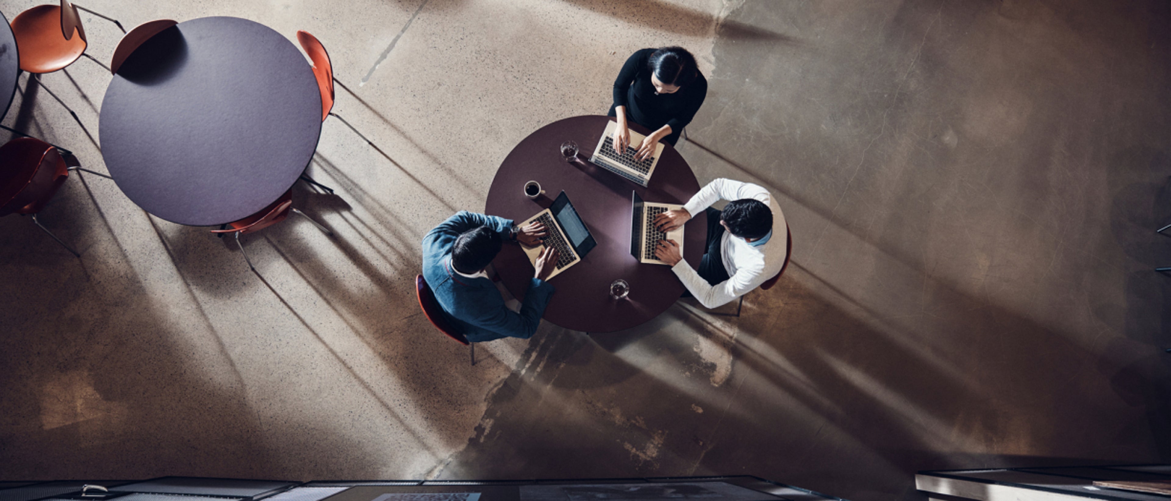 Three people sat around each other working on their laptops.