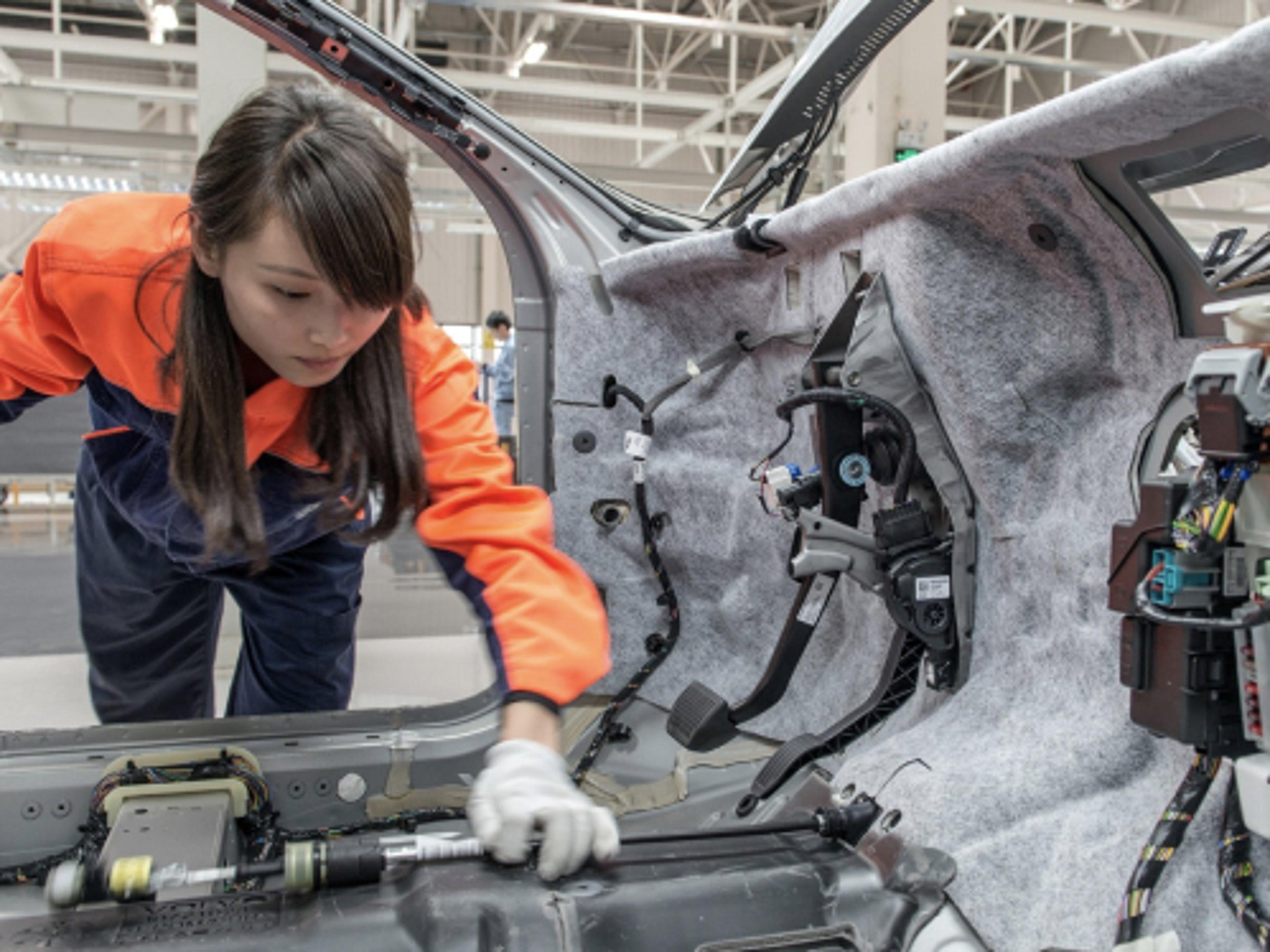 A woman examines the car's body in the factory.