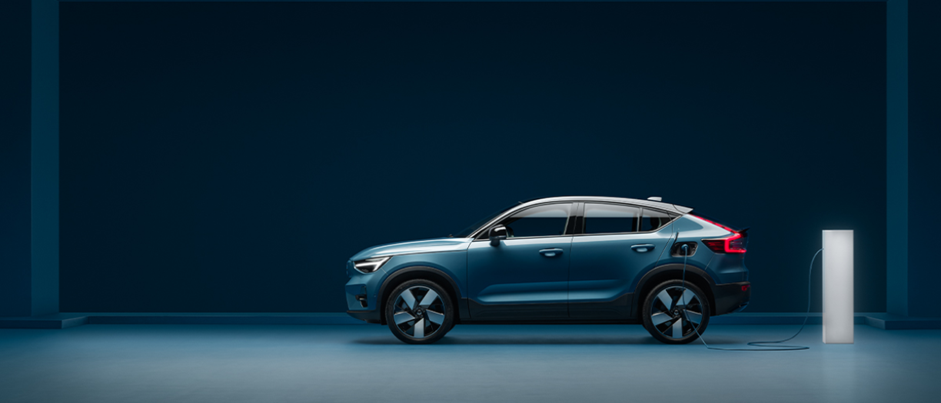 Side profile view of a Volvo C40 that’s charging inside a blue room.