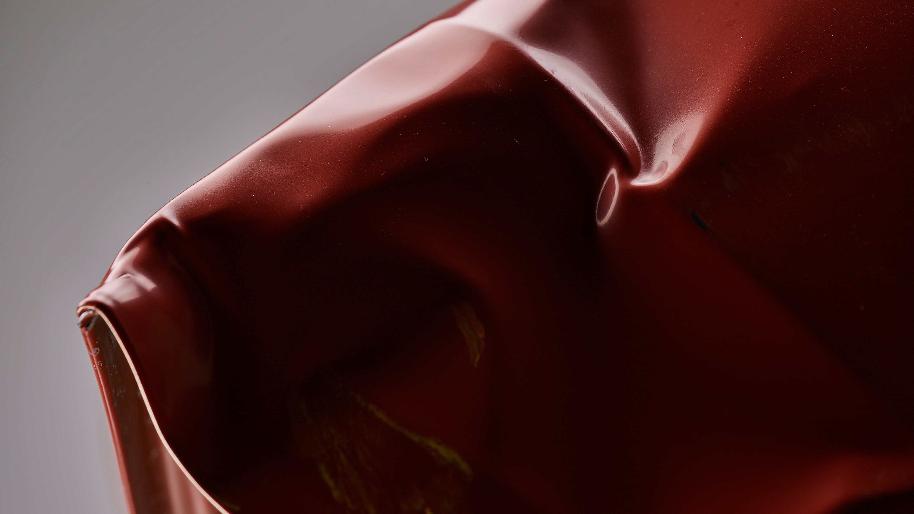 Close-up of dents and creases in glossy red car metal, showing impact damage with scuff marks.