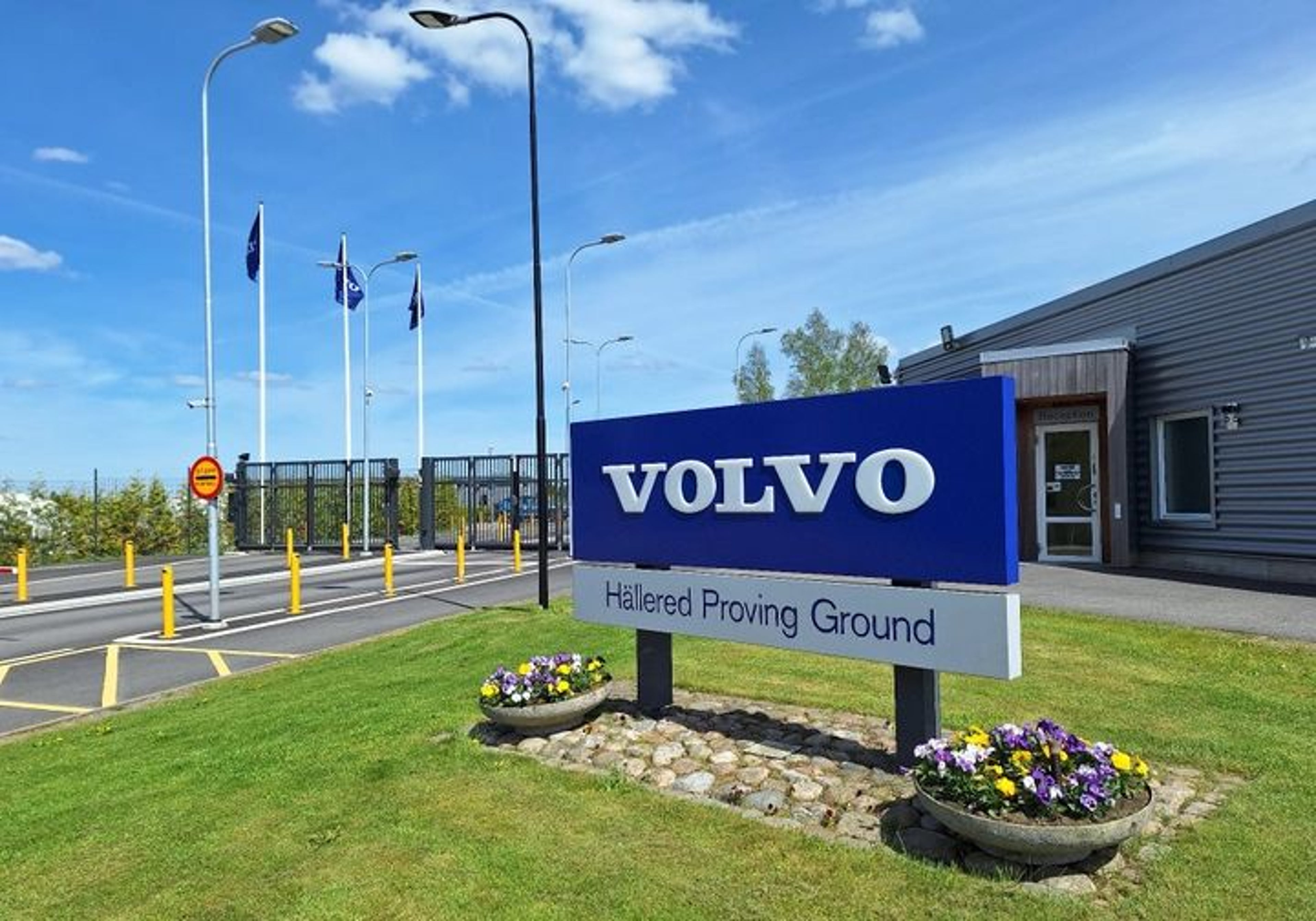 Entrance to the Volvo Hällered Proving Ground, featuring a large blue and white Volvo sign on a grassy area with flower planters.