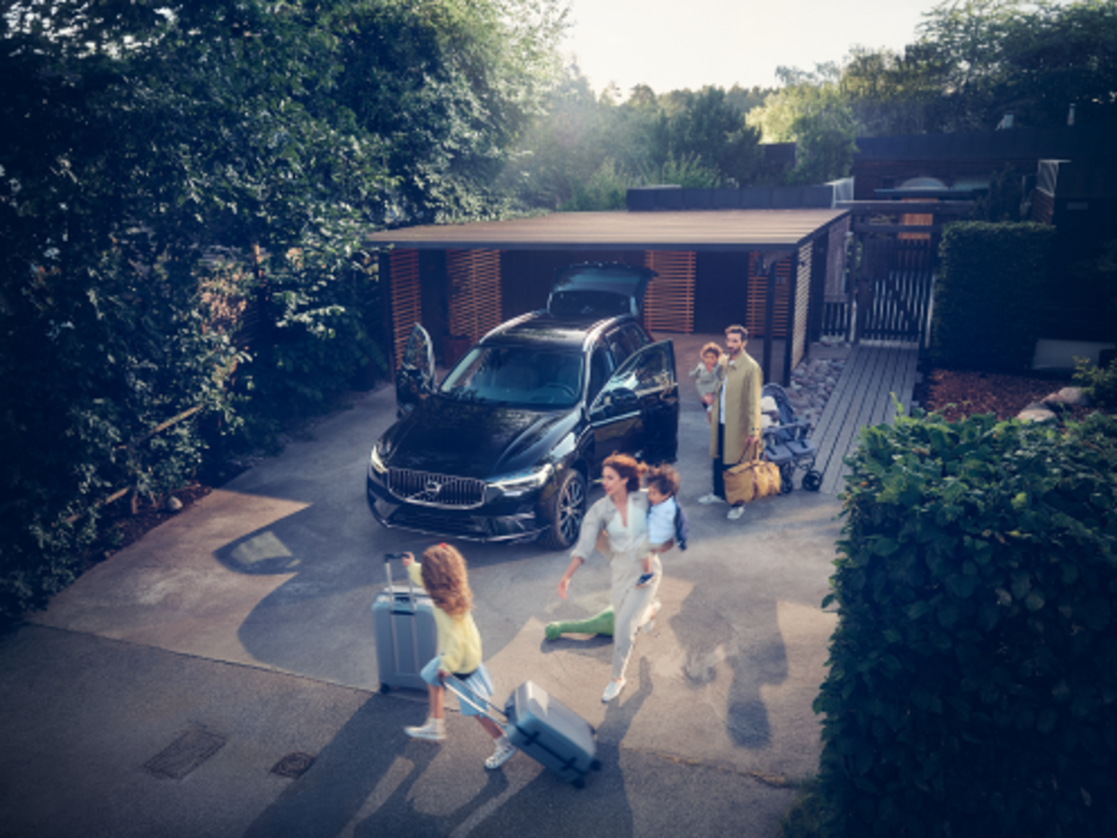 A family with 2 toddlers and luggage walking around a black Volvo car