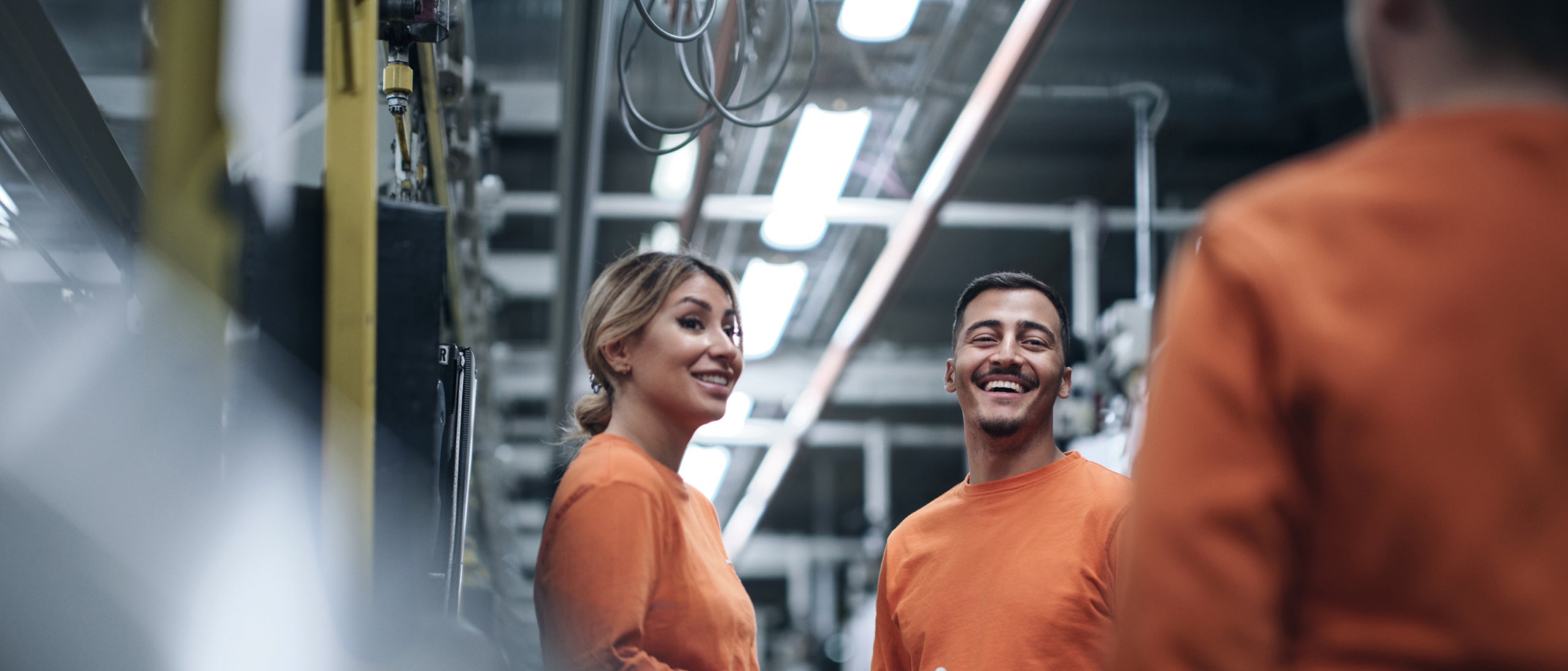 Trois personnes qui discutent à l'intérieur d'une usine de fabrication.