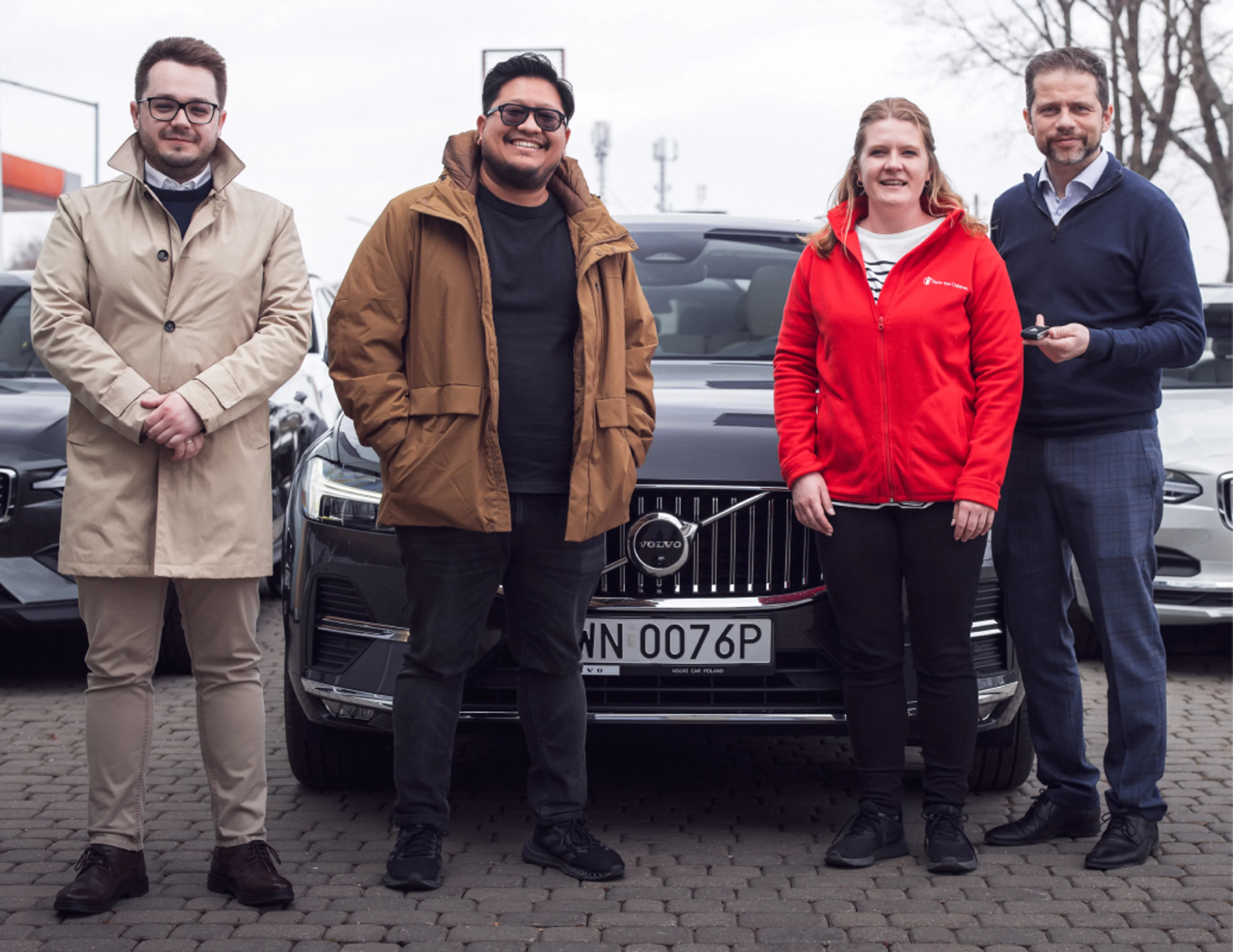 ثلاثة موظفين من شركة Volvo Cars أمام ثلاث سيارات فولفو يسلمون مفاتيح السيارة لامرأة من منظمة إنقاذ الطفولة.