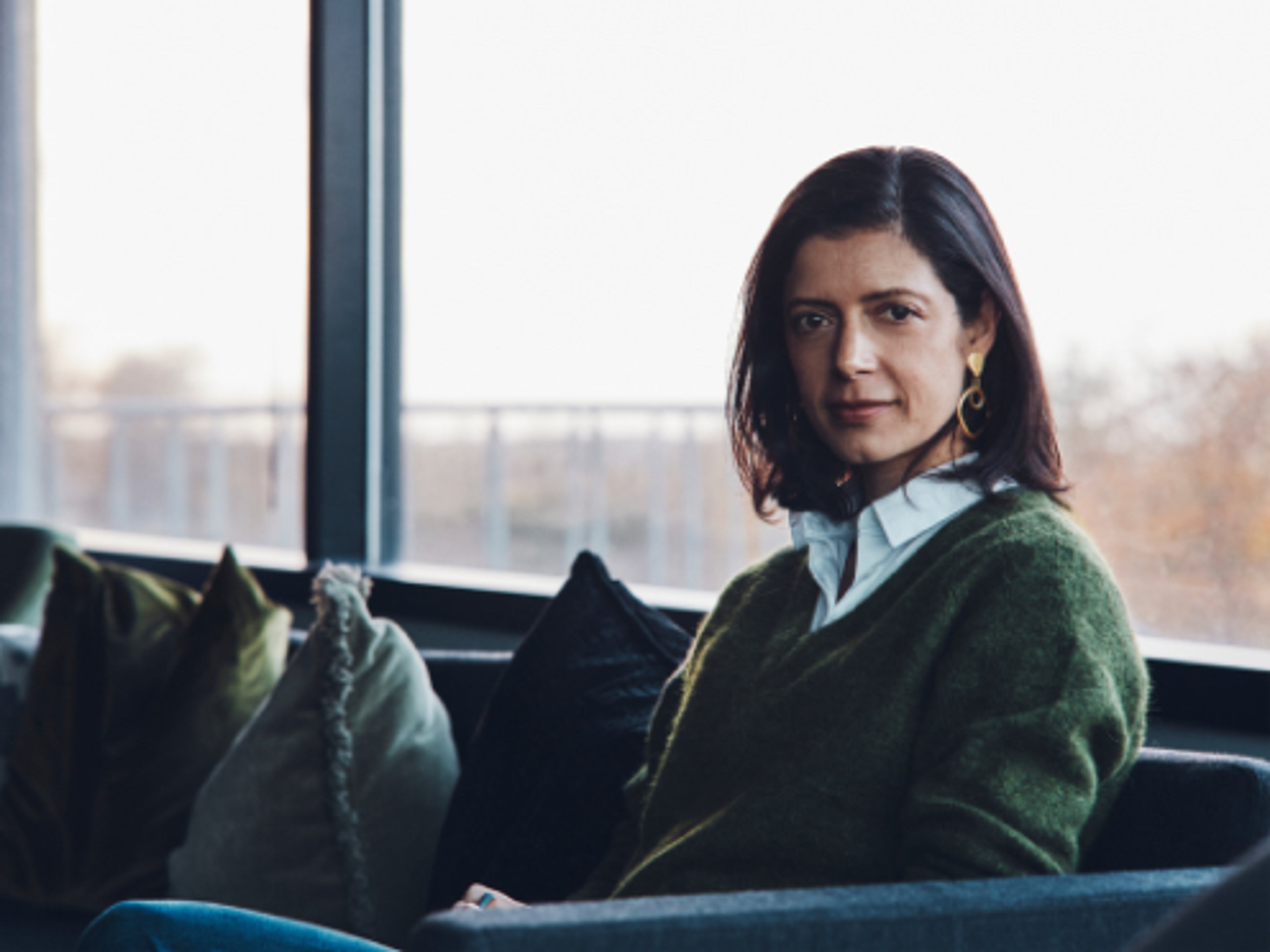 A woman sat on a sofa looking into the camera.