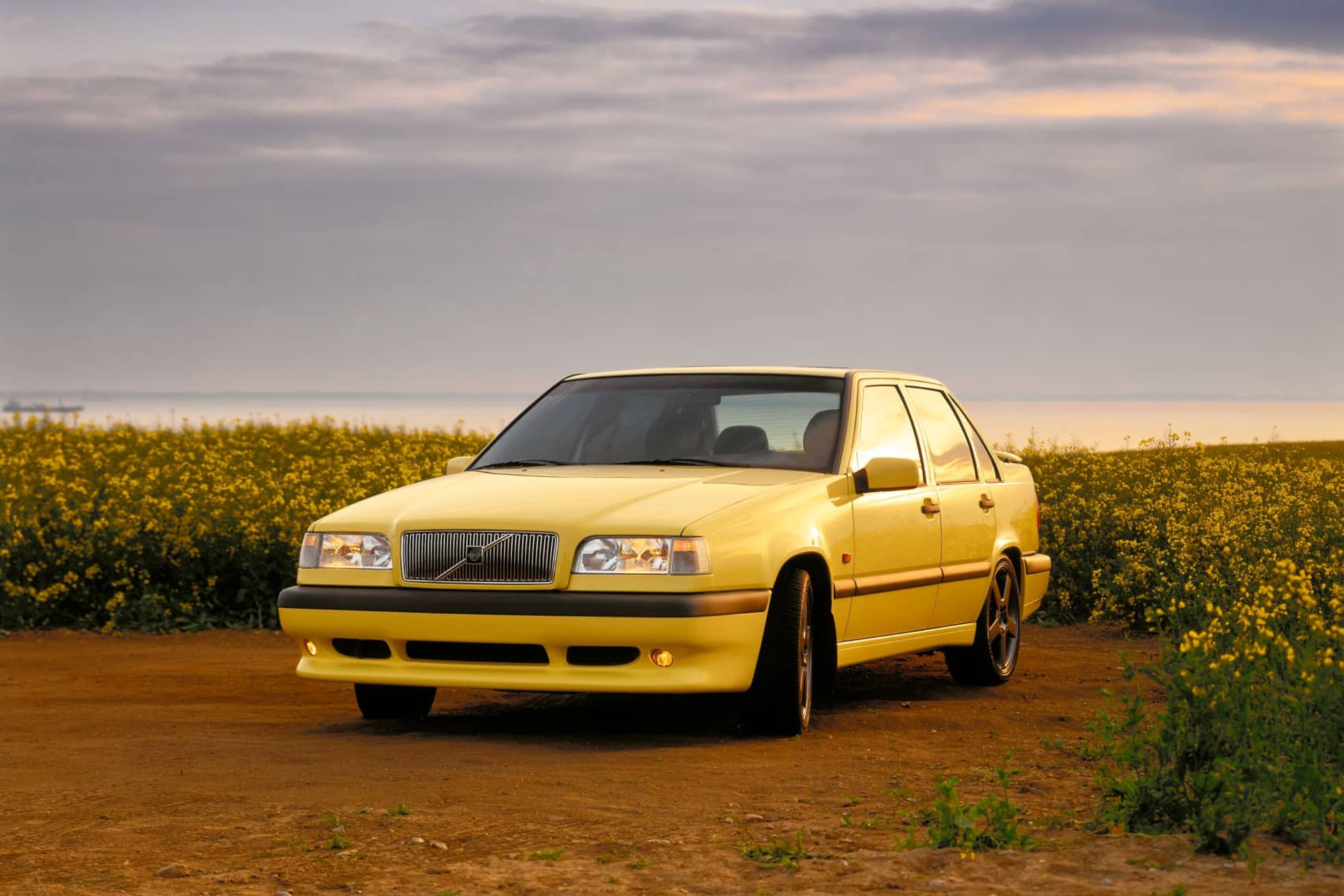 Un Volvo 850 amarillo aparcado frente a un campo de flores amarillas.