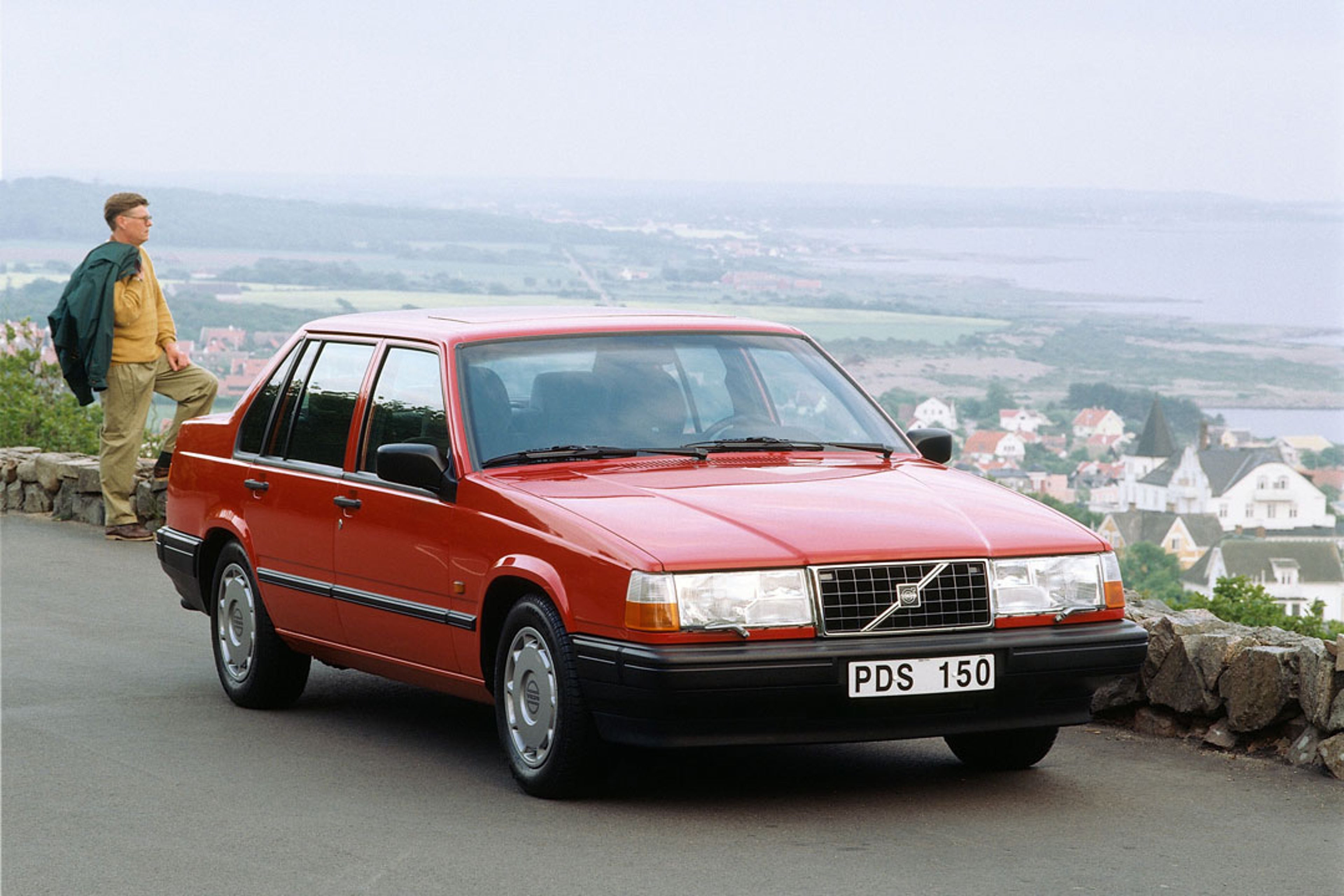 Un sedán Volvo 940 aparcado en una carretera junto a una colina.