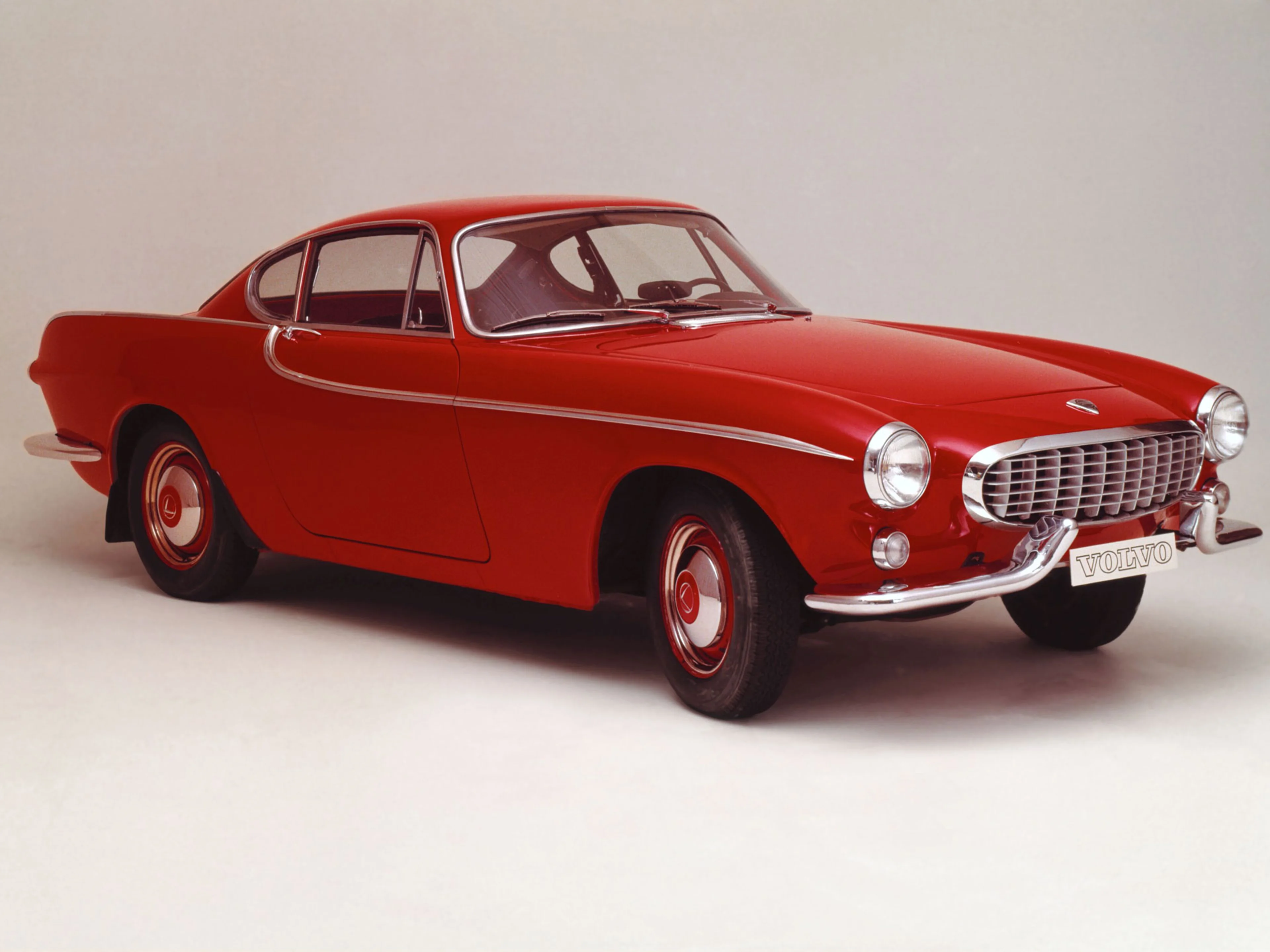 A classic red Volvo P1800 Convertible parked on a square.
