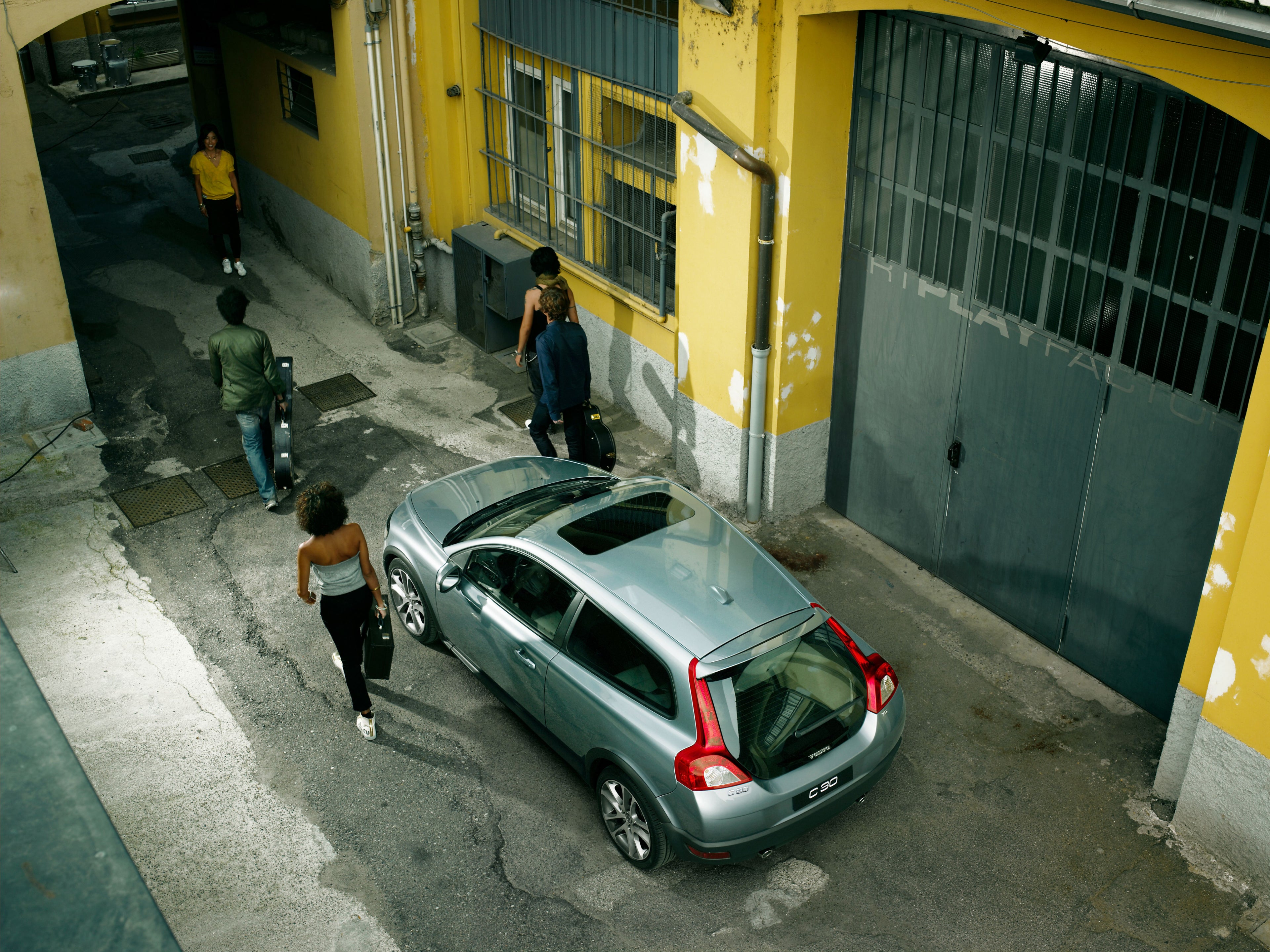 Una foto tomada desde arriba de un Volvo C30 estacionado en un entorno urbano con gente caminando a su lado.