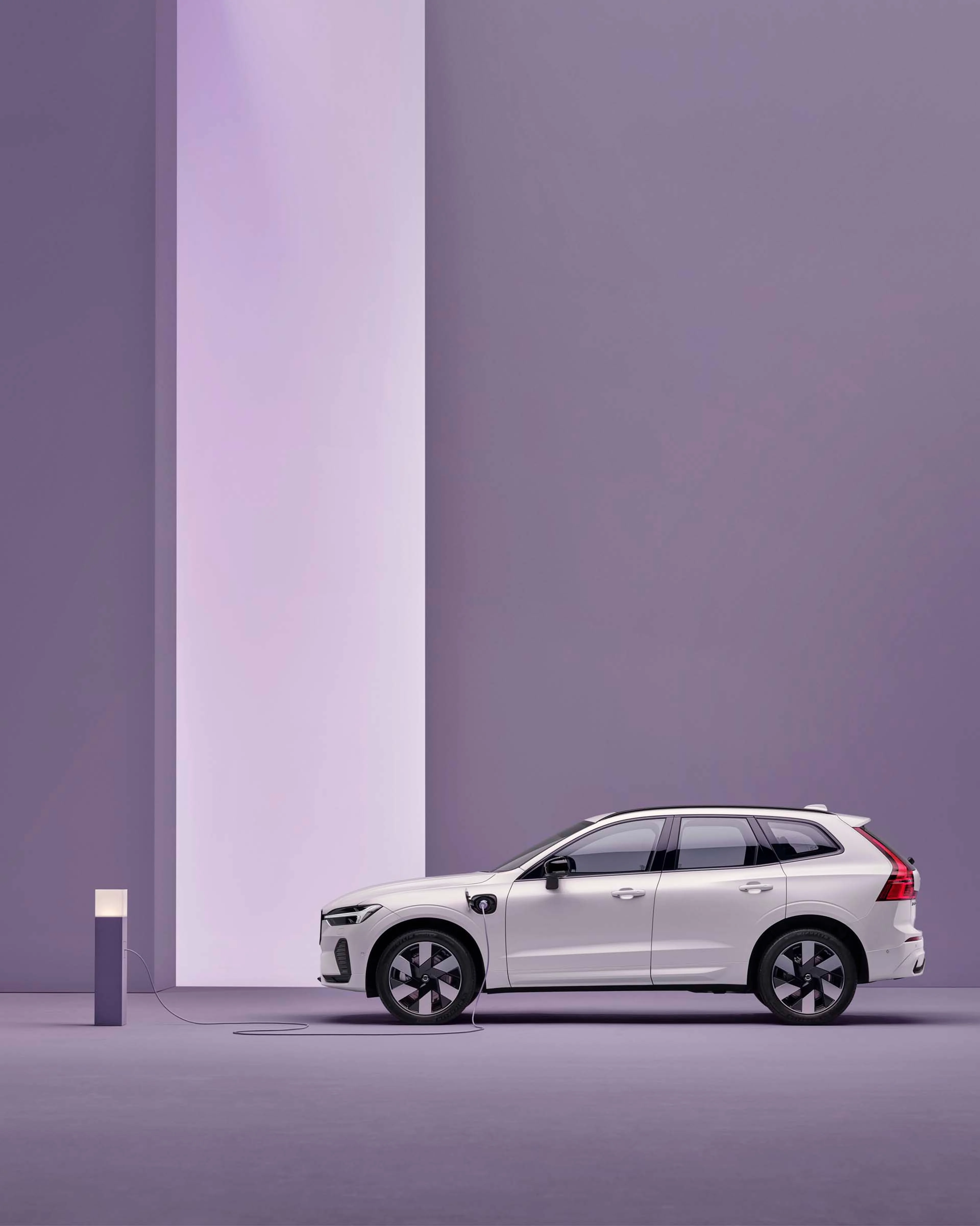 Vista lateral de un Volvo XC60 híbrido enchufable delante de un fondo morado.