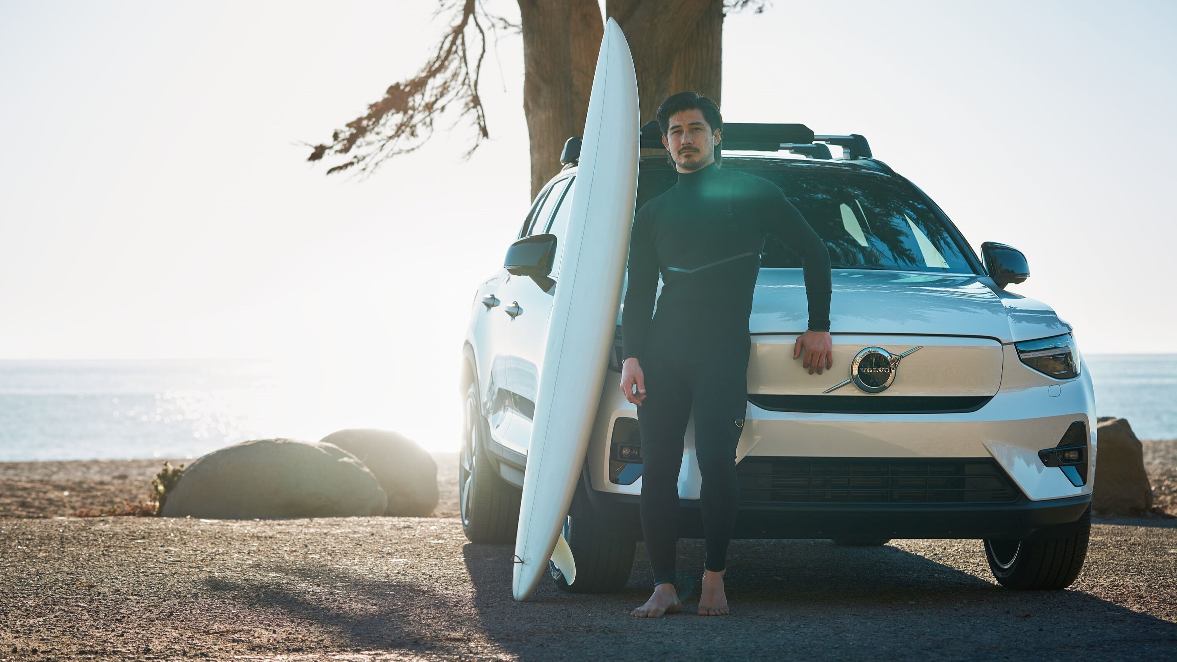man standing with surfboard next to Volvo EX40 fully electric SUV
