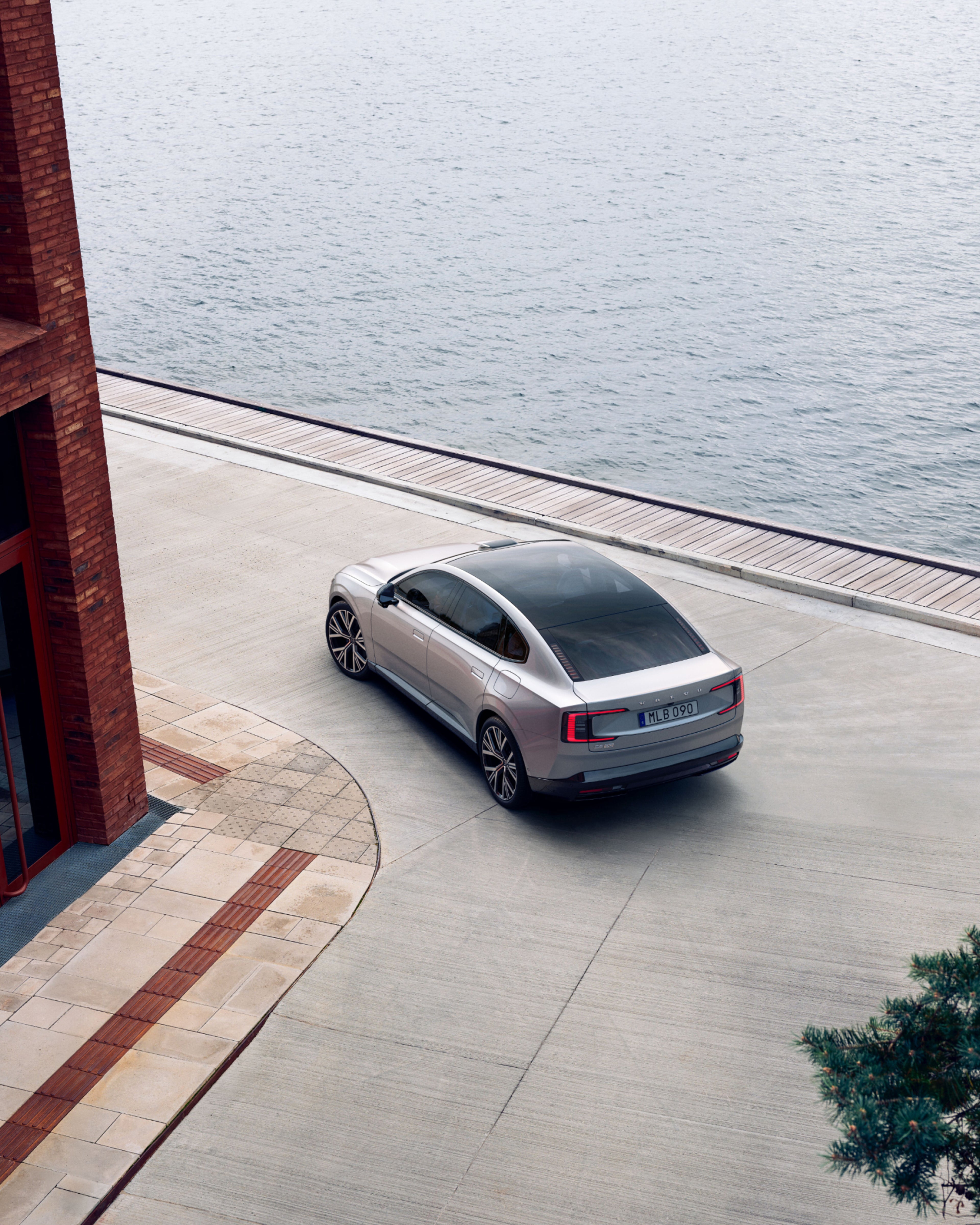 Vue arrière de la Volvo ES90 passant au bord de l’eau près d’un bâtiment en briques.