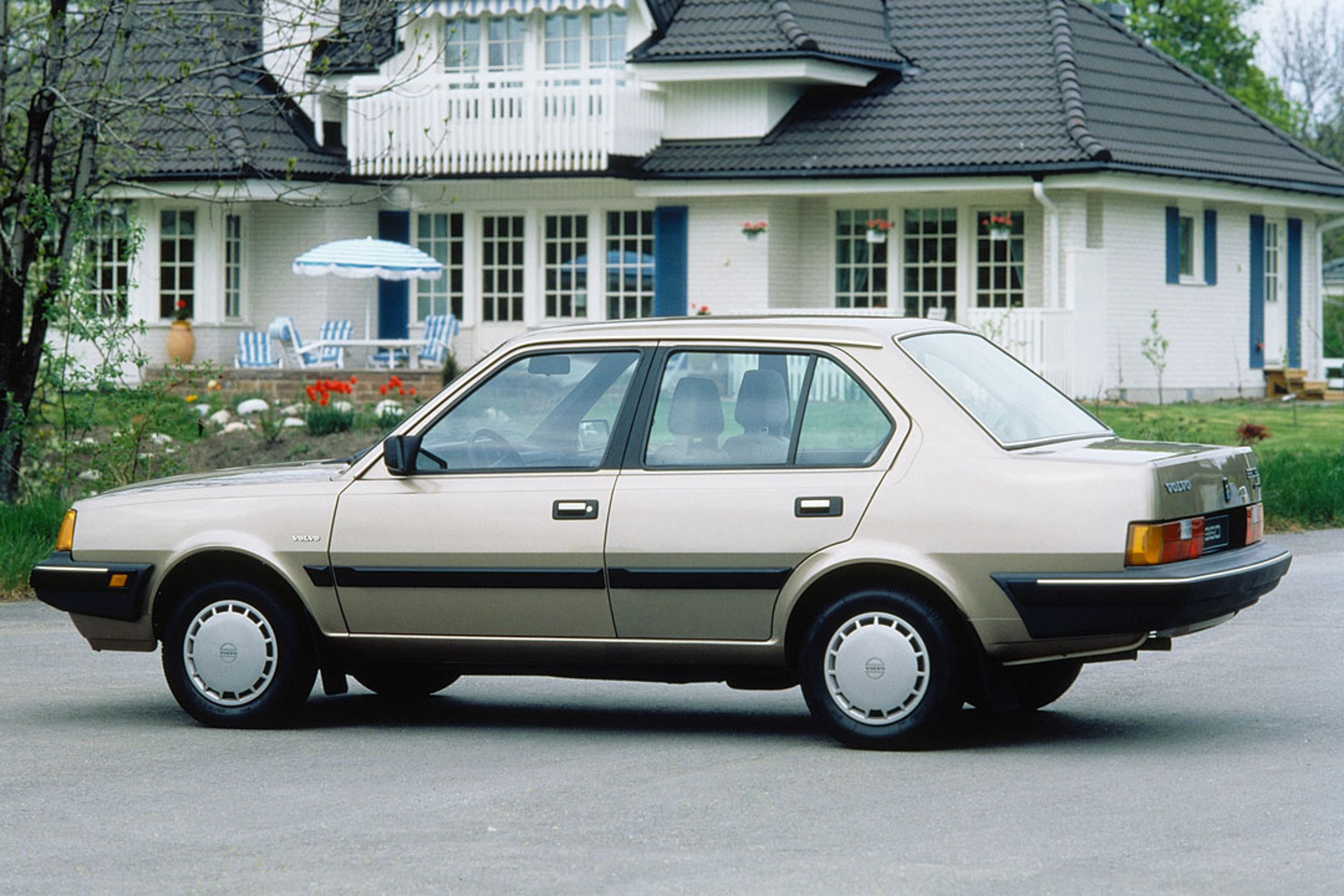 Un sedán Volvo 360 aparcado frente a una gran villa.