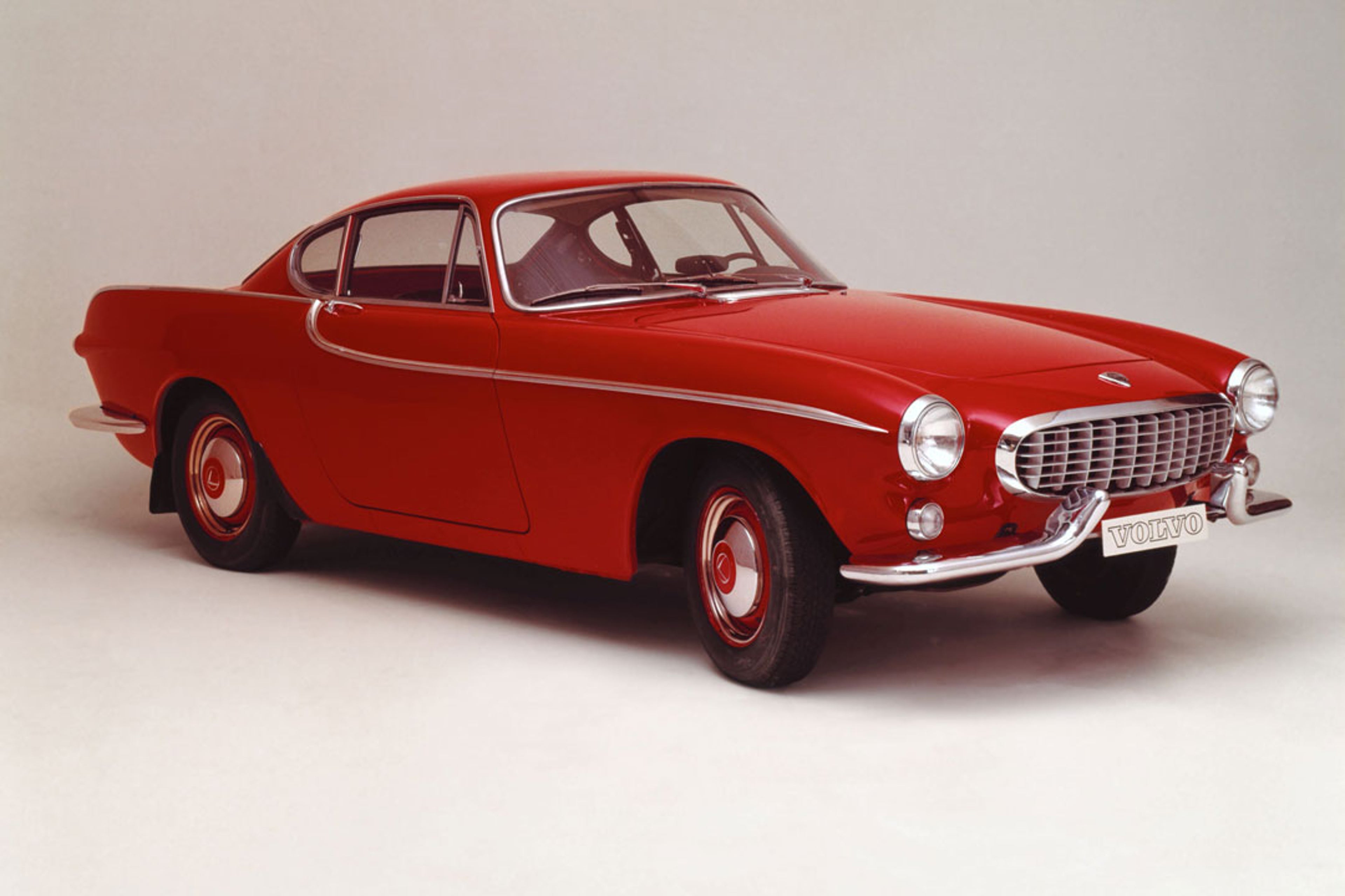 Un Volvo P130 Amazon rojo aparcado en un verde paisaje montañoso.