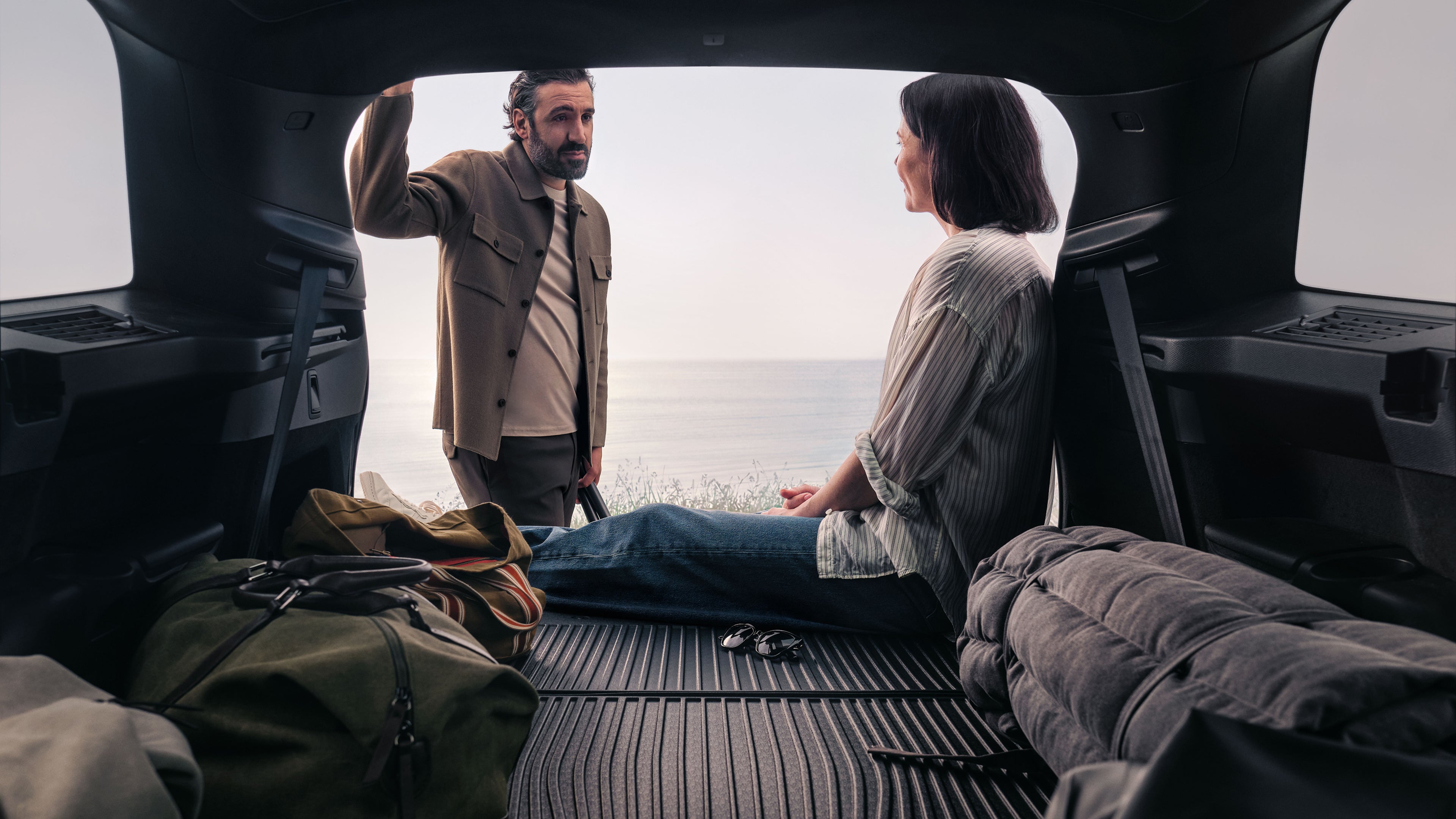 Volvo XC90のラゲッジスペースに座っている女性とその傍らに立つ男性