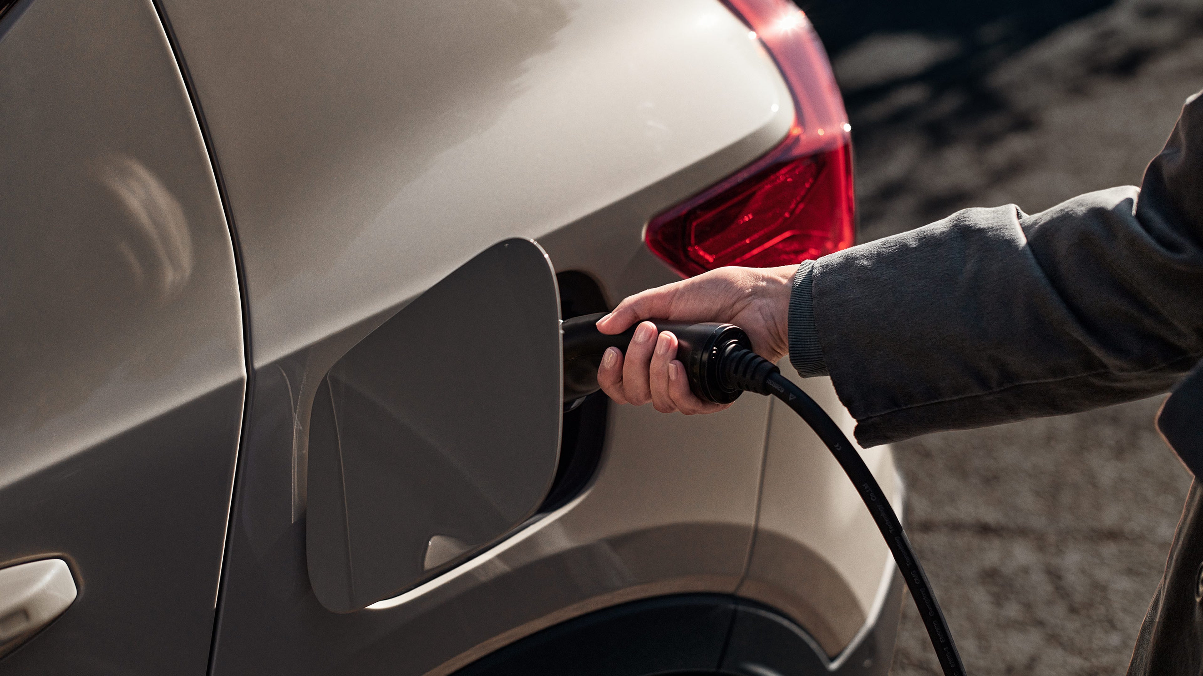 Lähikuva Sand dune -värisen Volvo EX40 täyssähköisen katumaasturin latauspistorasiasta, johon nainen on juuri kytkemässä latauspistoketta.