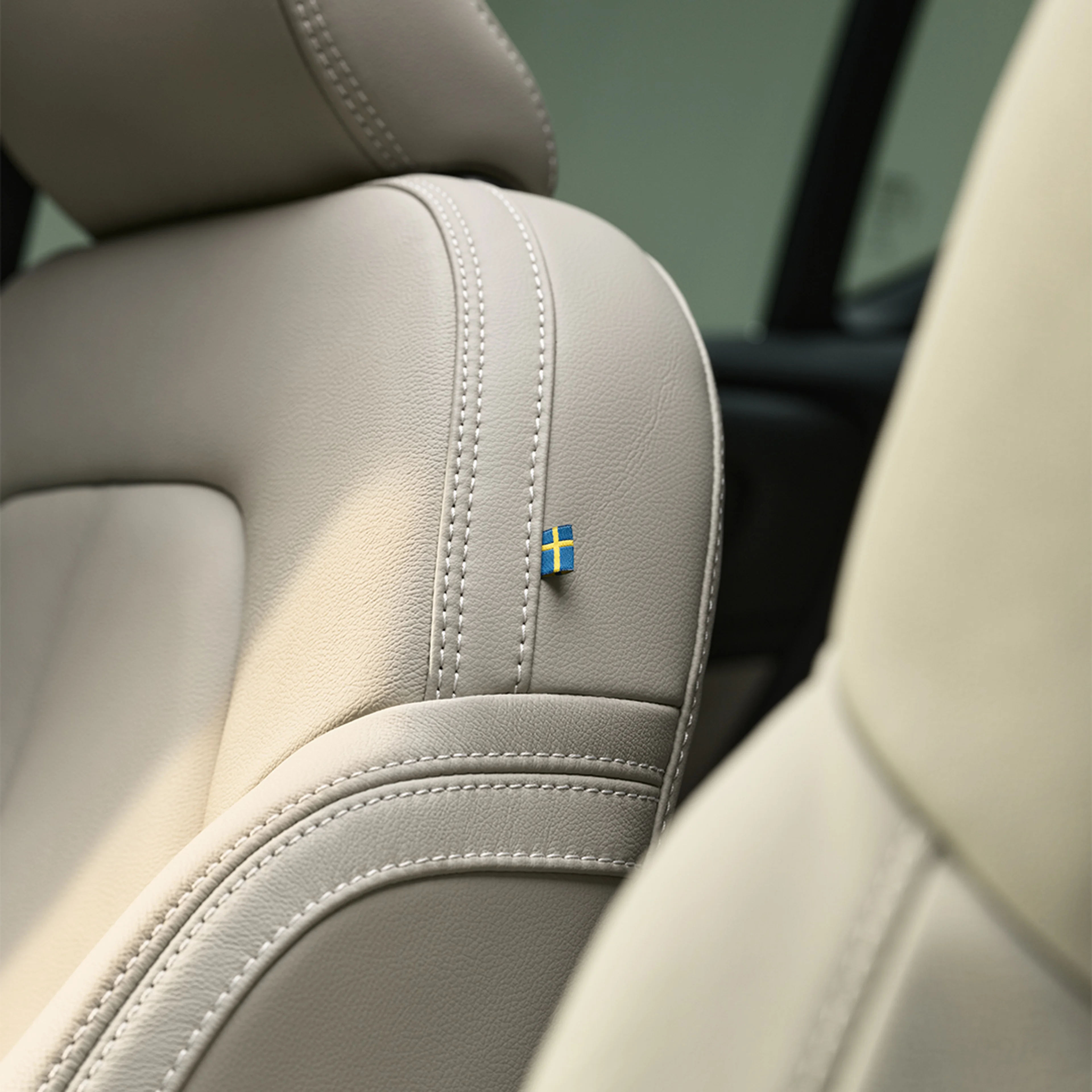 Detalle de las costuras del asiento de piel del pasajero delantero del Volvo XC40 semihíbrido con una pequeña bandera sueca.