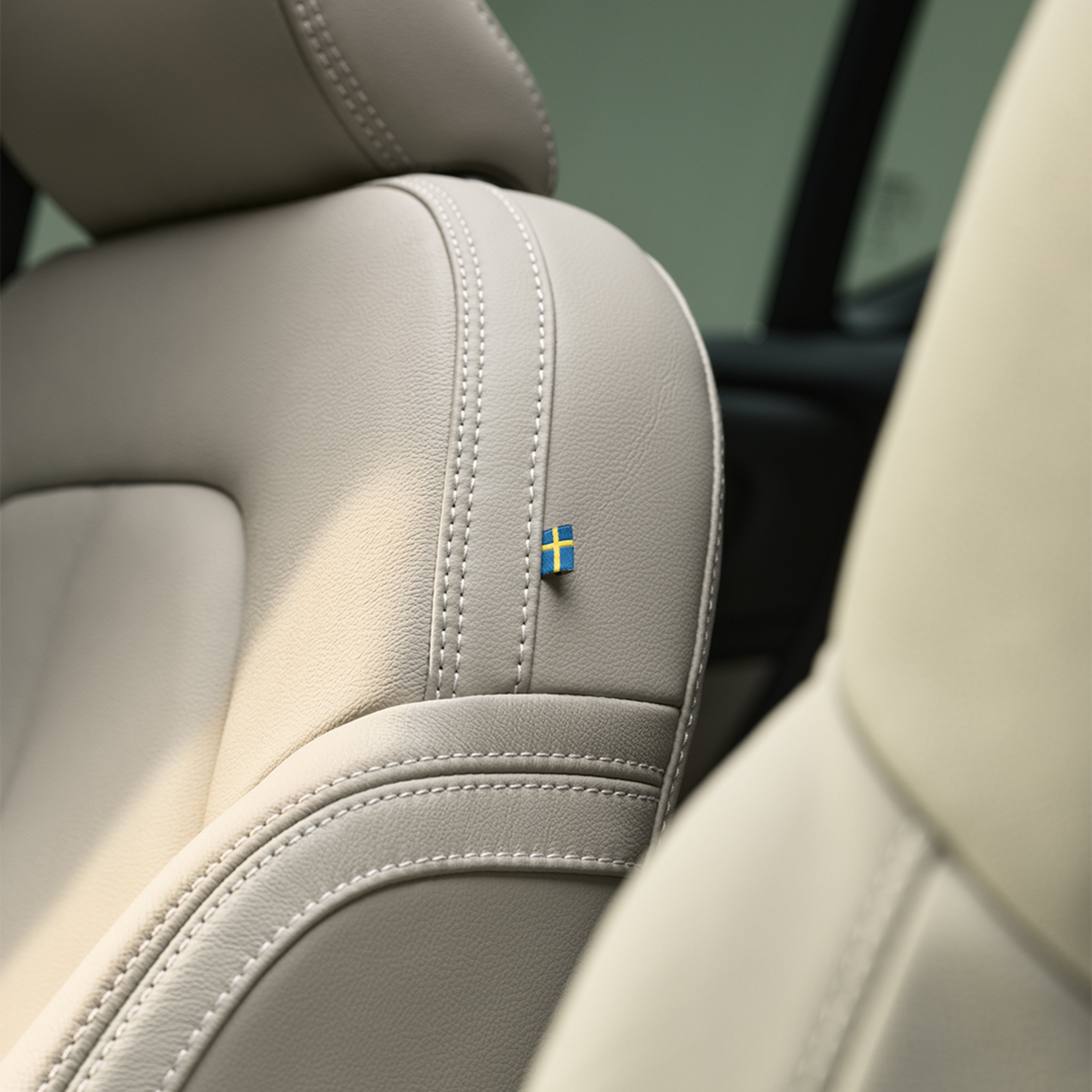 Detalle de las costuras del asiento de piel del pasajero delantero del Volvo XC40 semihíbrido con una pequeña bandera sueca.