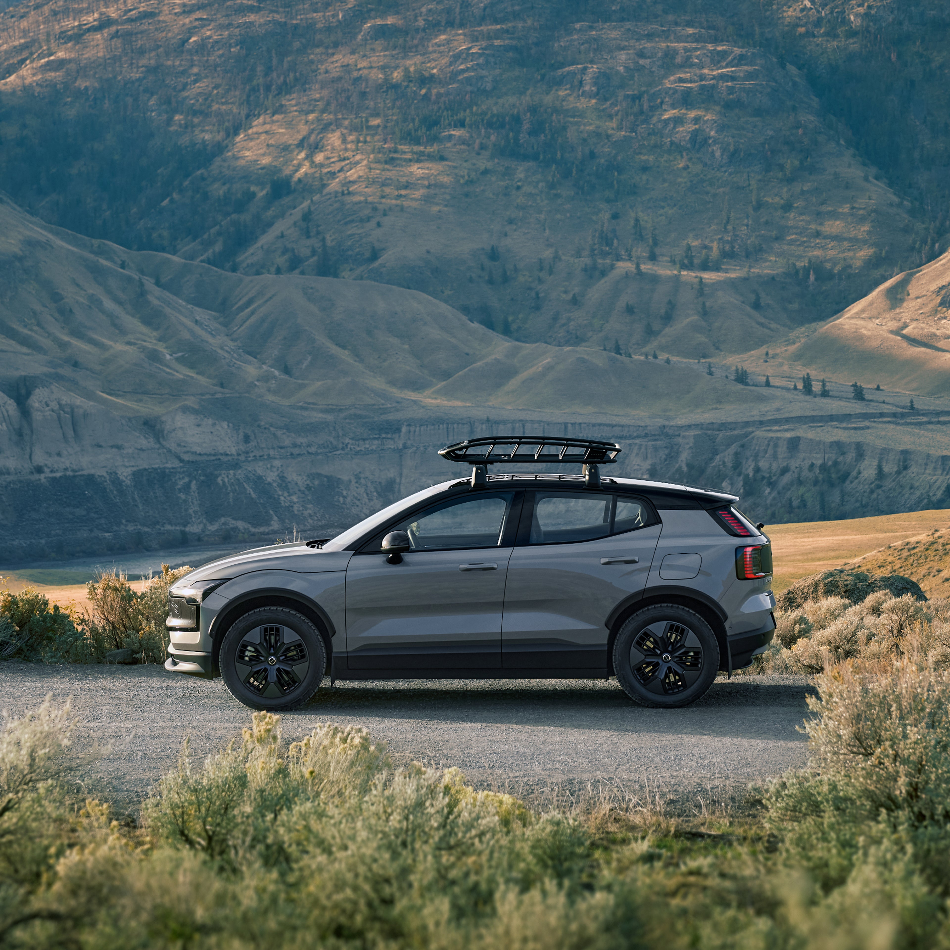 La EX30 Cross Country avec un panier de rangement pour toit vue de côté dans un environnement vallonné.