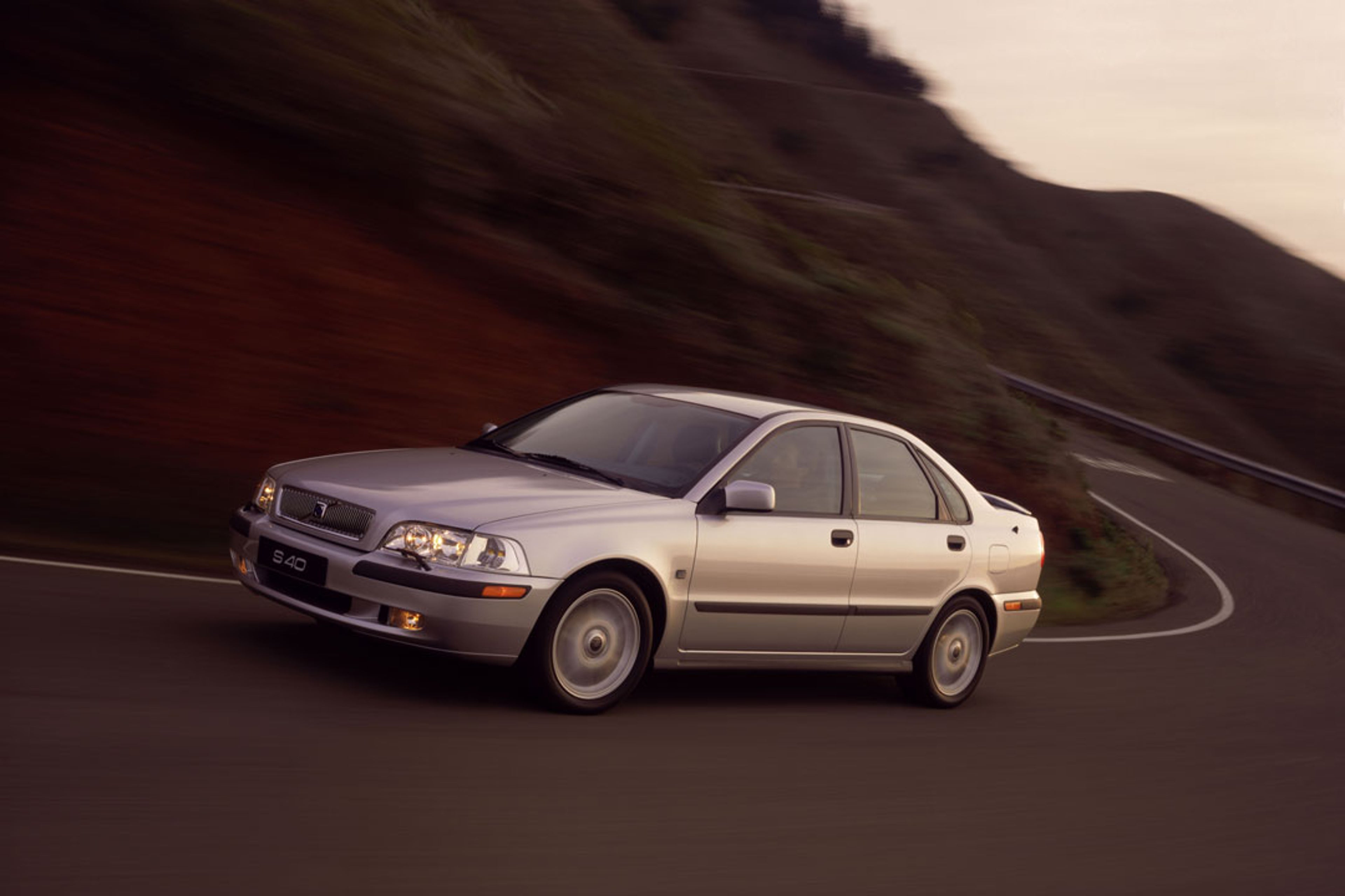 Un sedán Volvo S40 circulando por una carretera junto a una colina.